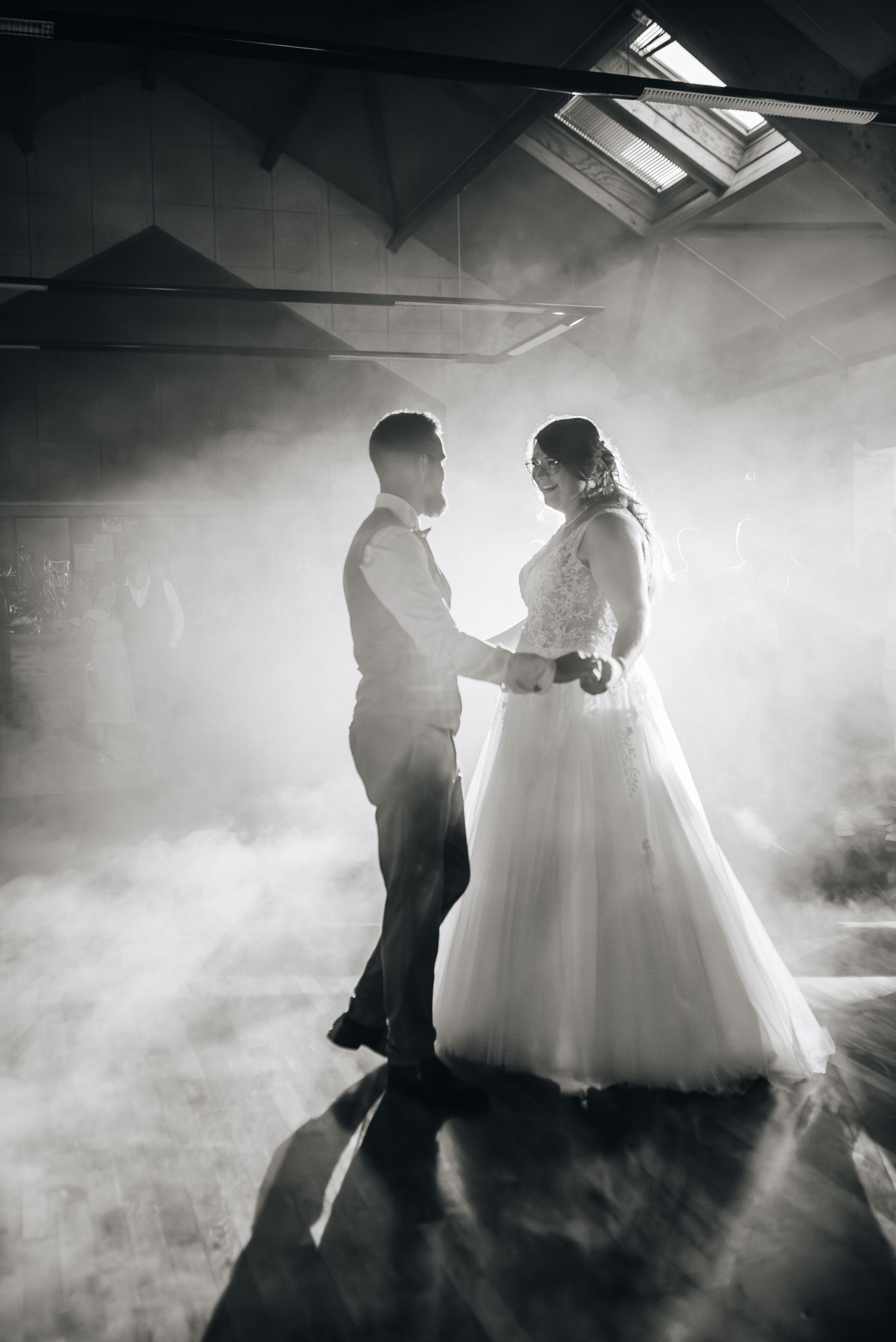 Atmospheric silhouettes of a couple dancing in fog with dramatic backlighting through skylights.