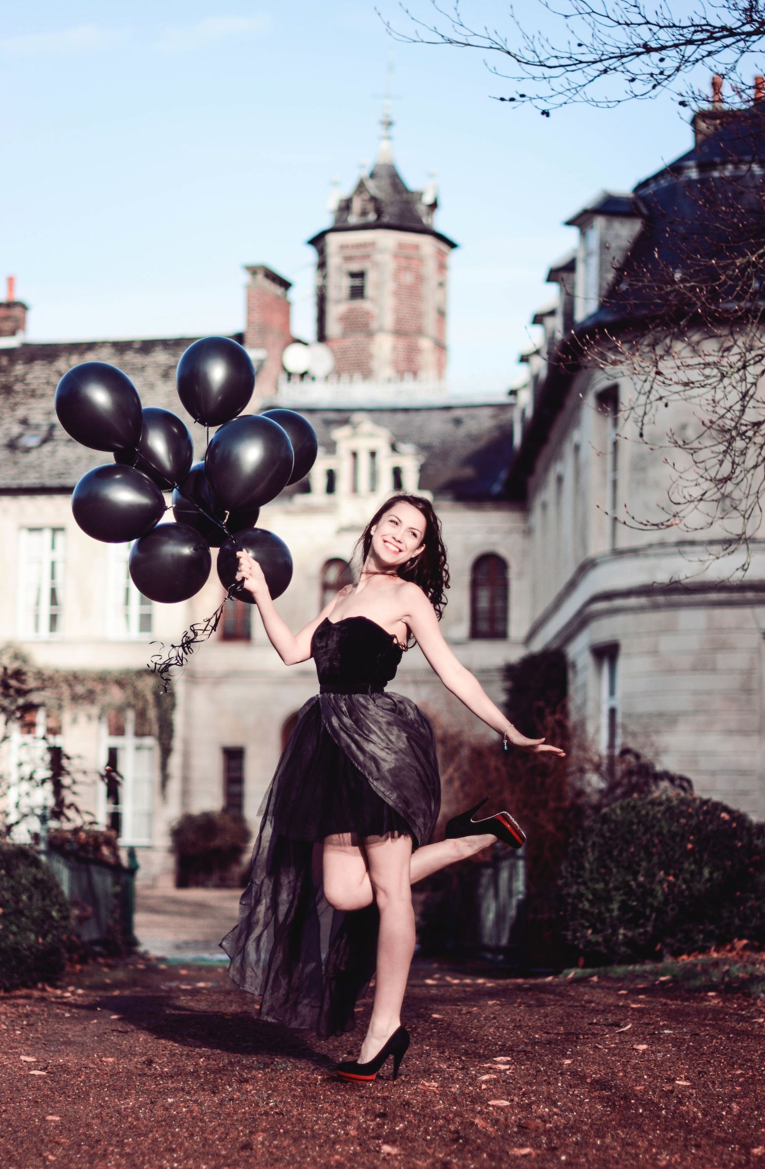Whimsical fashion shot with black balloons and tulle dress against historic building backdrop.