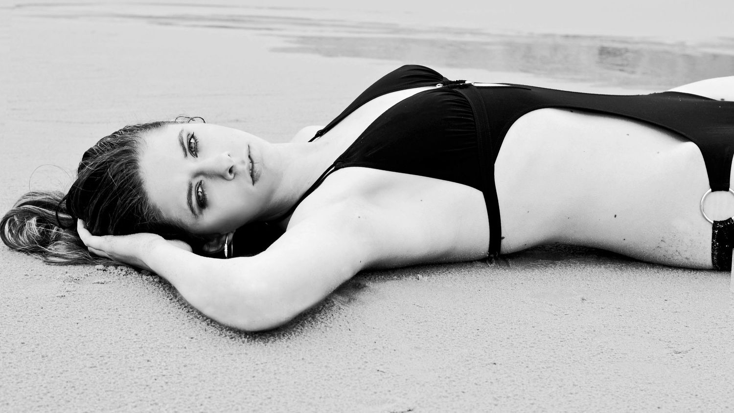 Black and white portrait of someone lying on beach sand in a classic swimsuit.