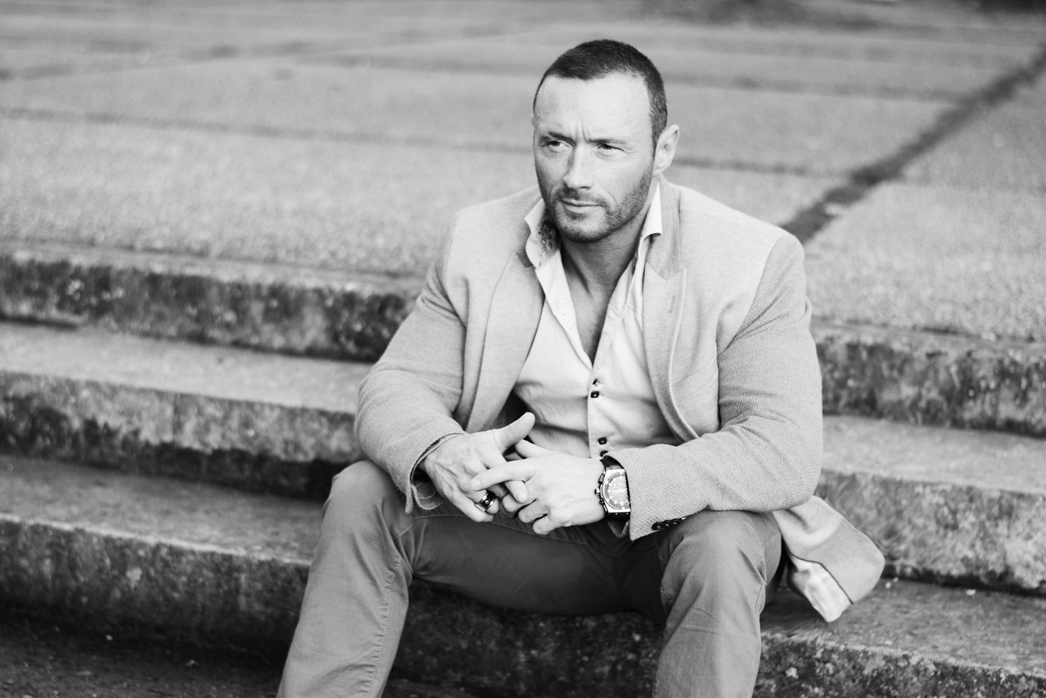 Black and white photo of person sitting on concrete steps wearing casual attire.
