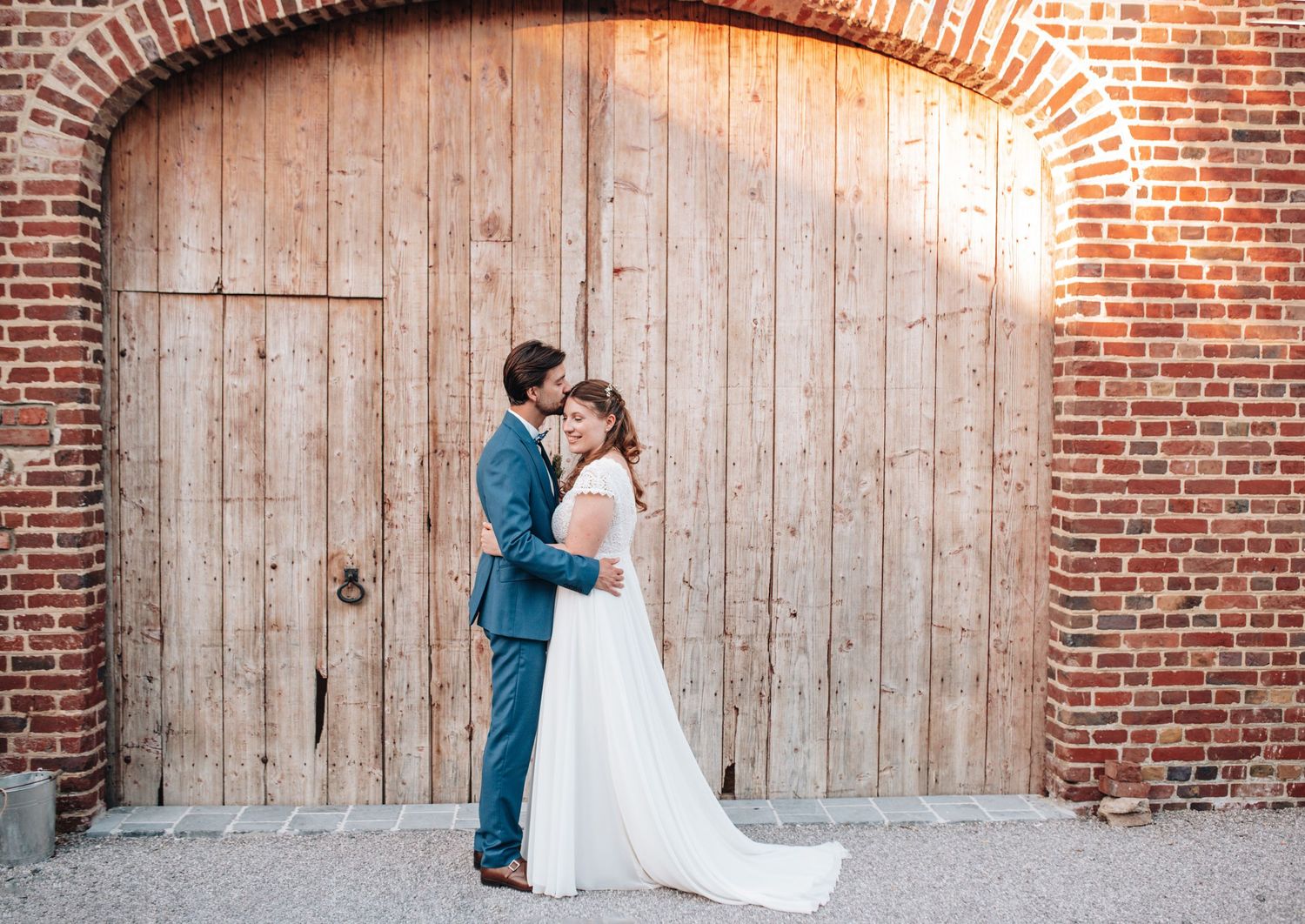 A couple shares an intimate moment against a rustic brick wall and wooden backdrop.