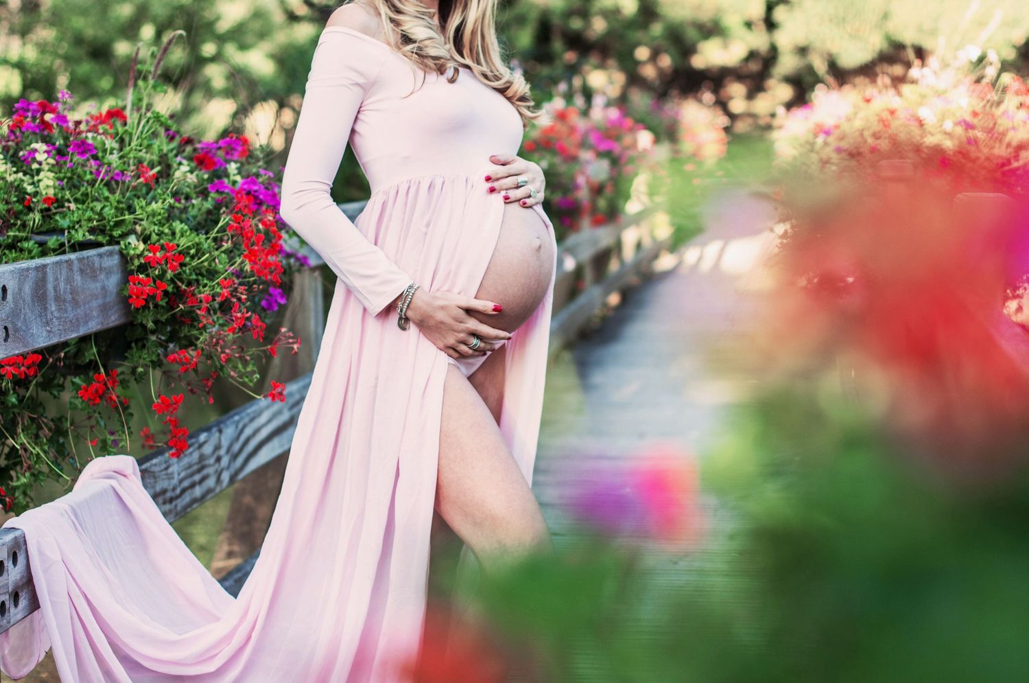 Romantic maternity photos in a garden with pink dress and blooming flowers.