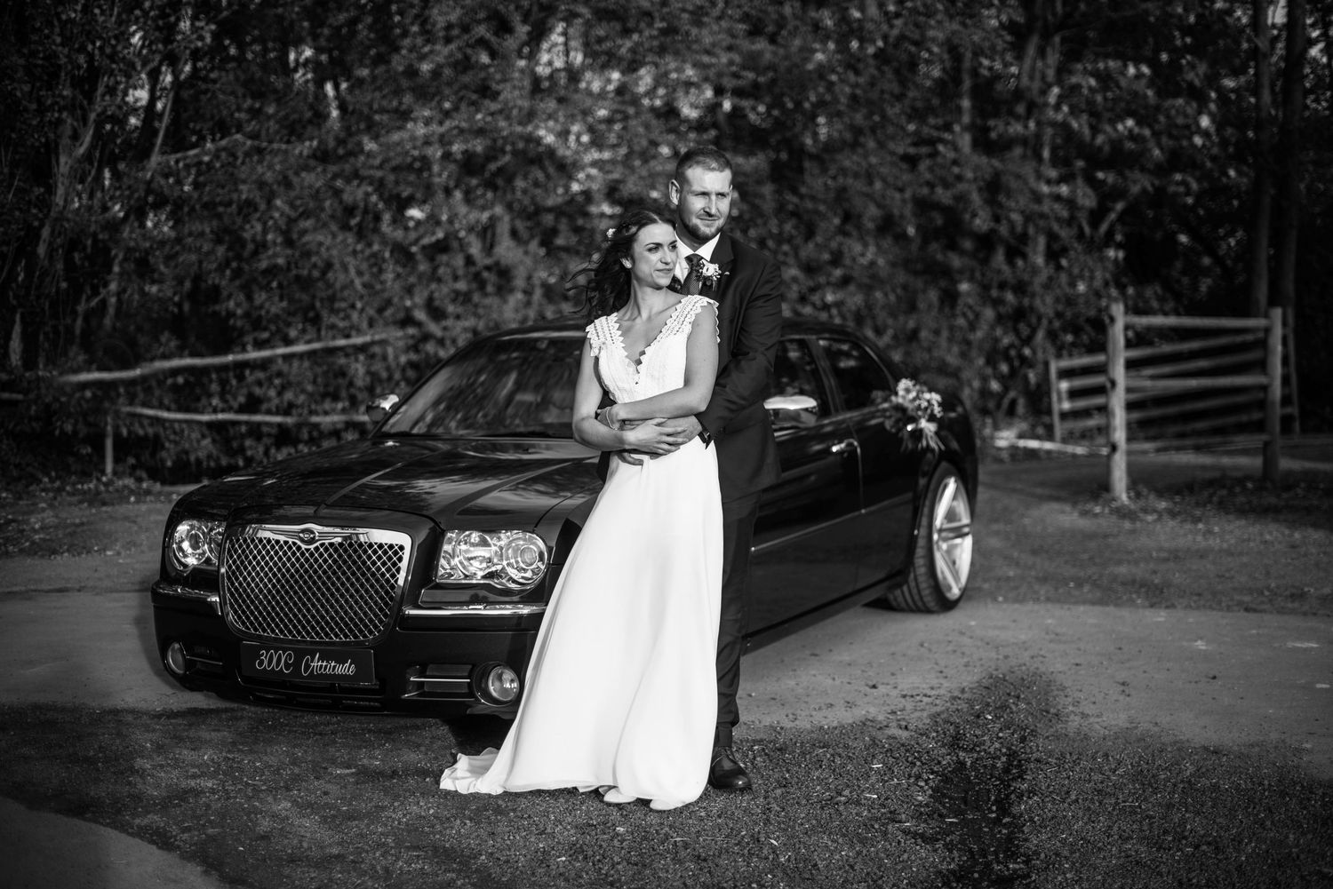 Wedding couple poses near vintage black car in outdoor setting.