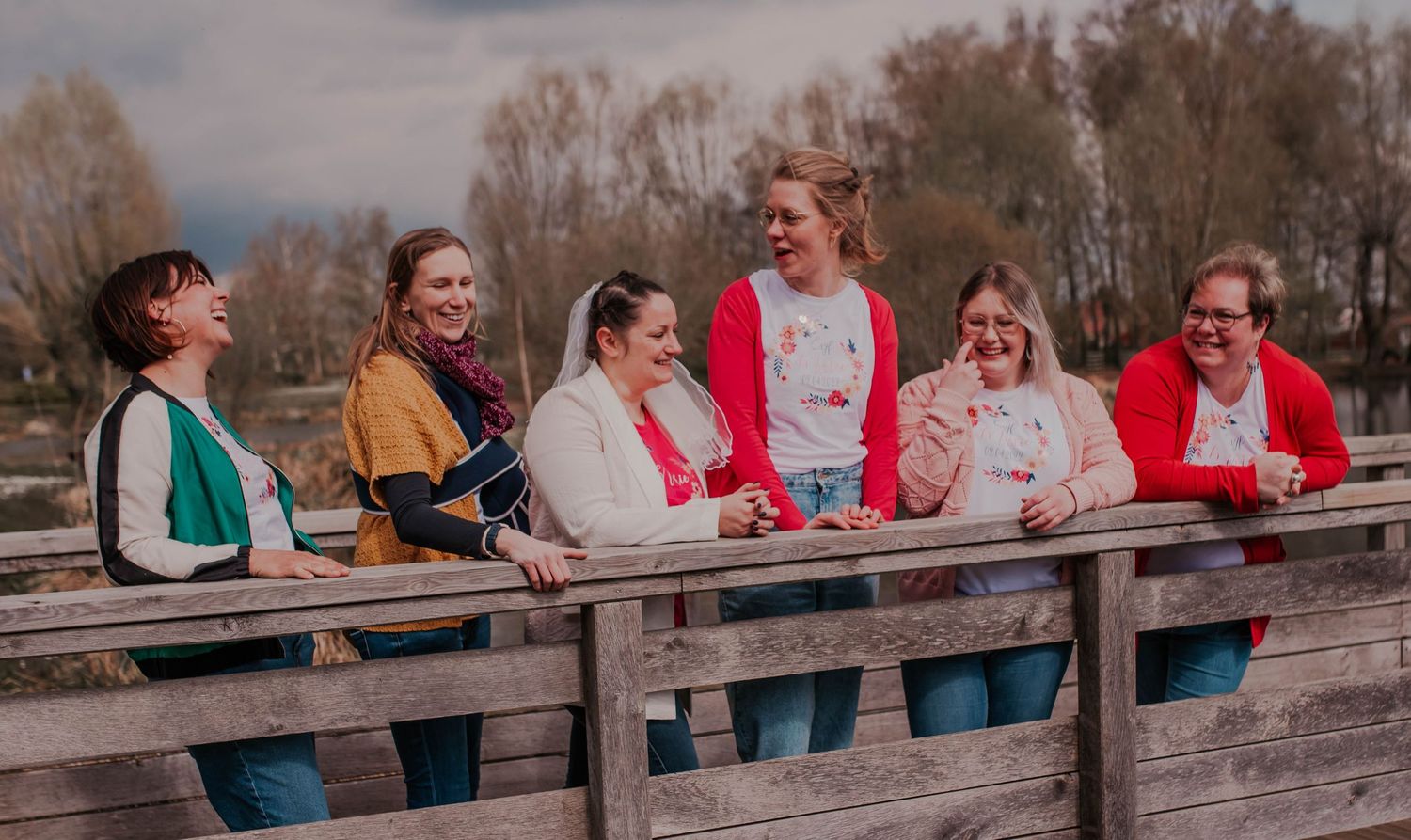 Friends posing and laughing together on a wooden bridge during an outdoor photoshoot.