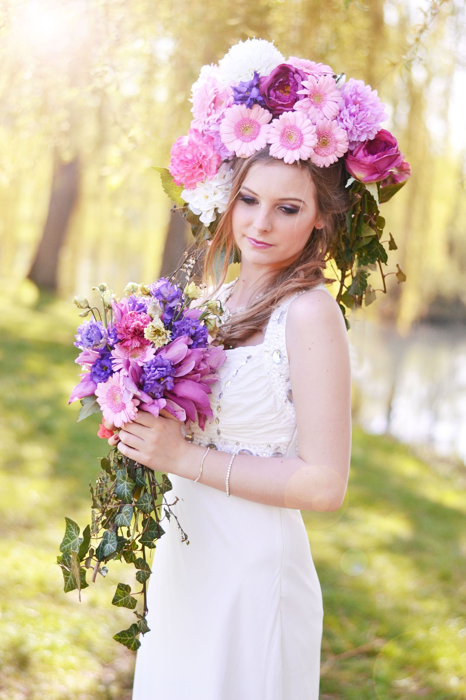 Ethereal spring photoshoot with floral crown and white dress in a sunlit forest setting.