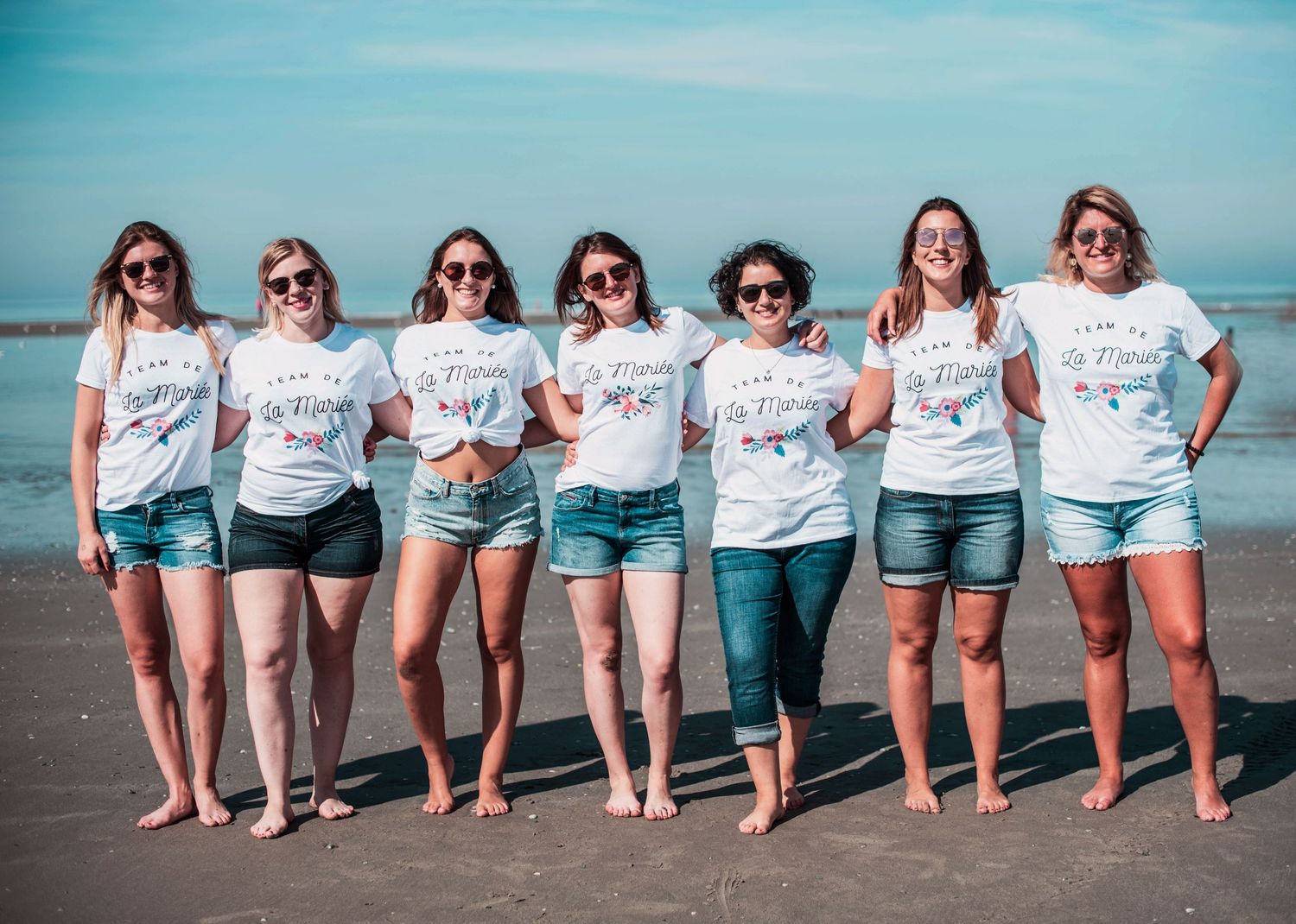 Group of friends in matching outfits posing playfully on beach shoreline.