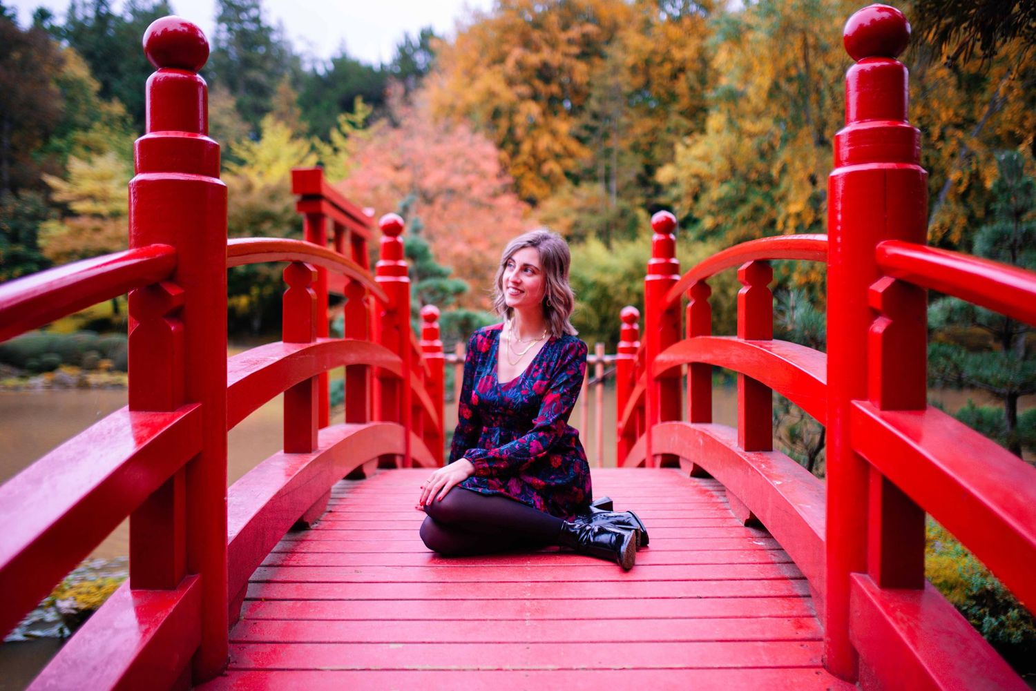 Red Japanese bridge in a garden with vibrant autumn foliage.