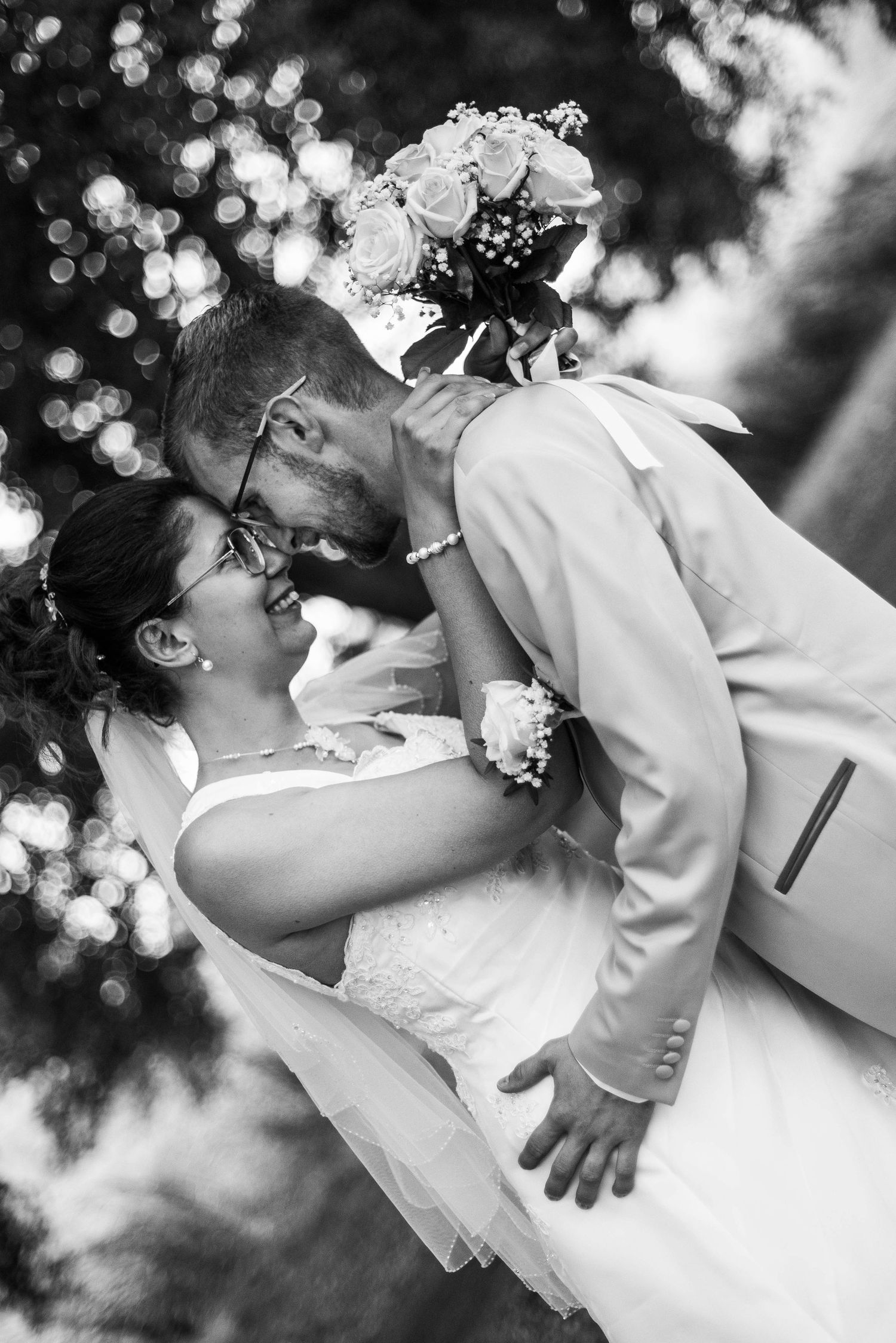 A romantic black and white wedding photo showing a couple in an intimate dip pose with bokeh lighting effects.