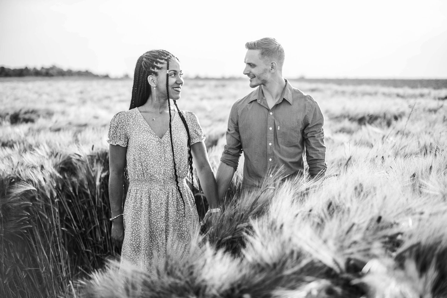 Black and white portrait of couple walking through tall wheat field.