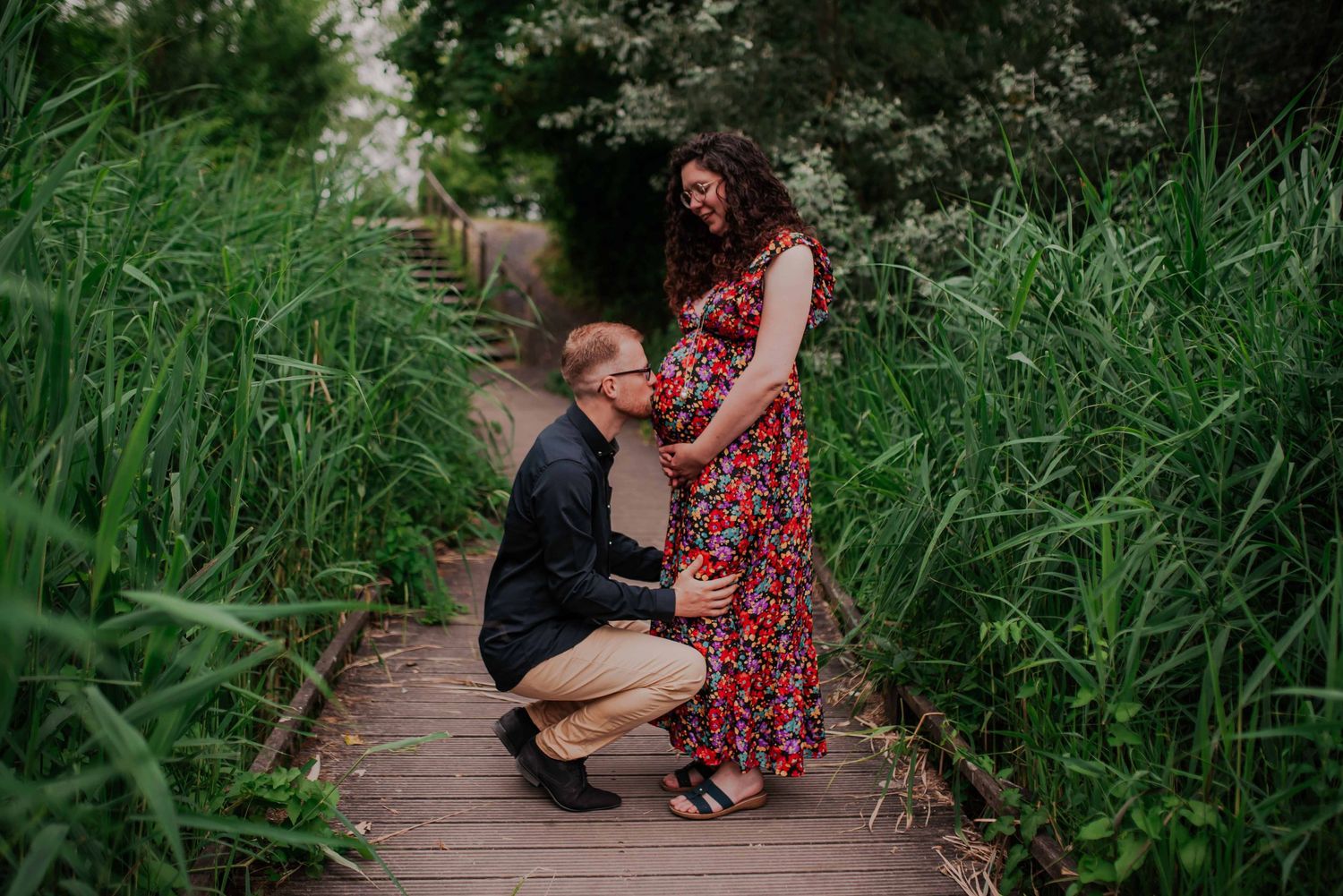 A tender moment captured on a wooden boardwalk surrounded by lush greenery.