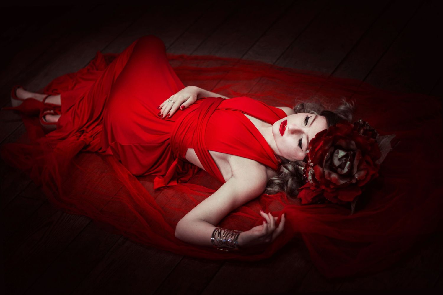 Dramatic portrait of someone lying in red dress against dark background with moody lighting.