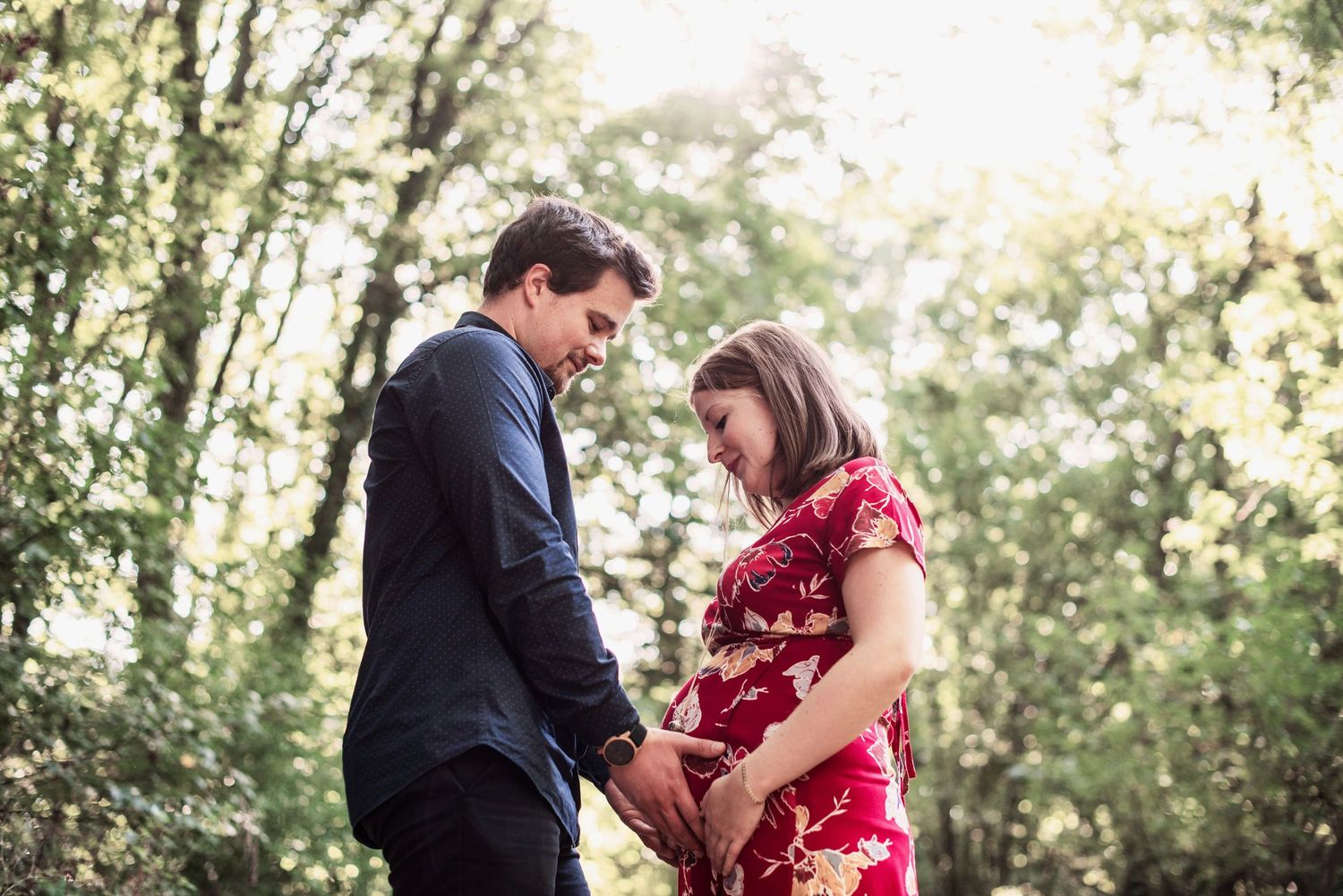 Intimate maternity moment captured in a sunlit forest setting.