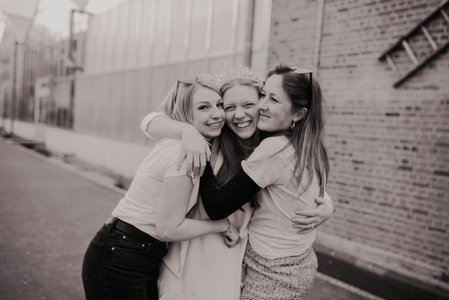 Three friends share an intimate embrace in a black and white street photo.