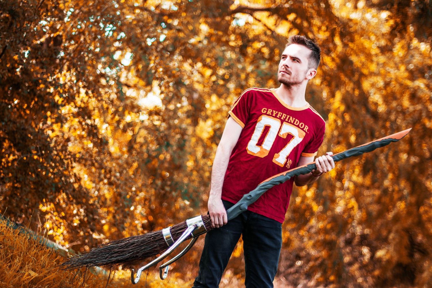 A person in a red shirt holds a broomstick against an autumn background with golden foliage.