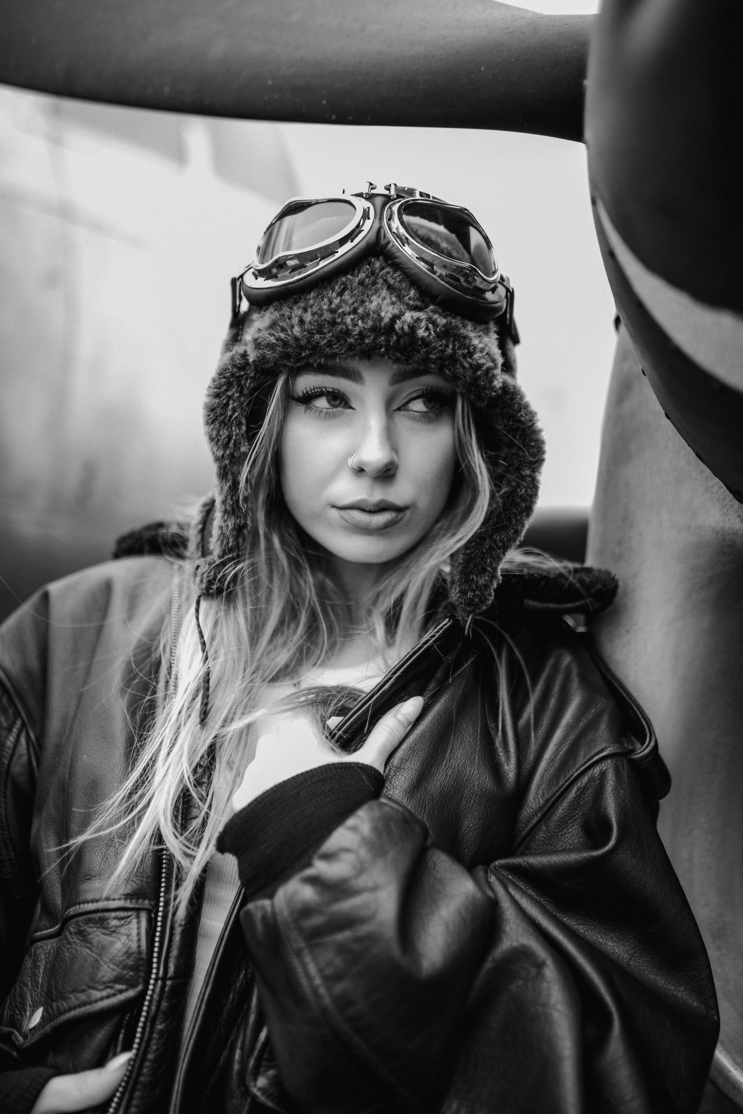 Retro aviation-themed portrait with leather jacket and vintage pilot goggles in black and white.
