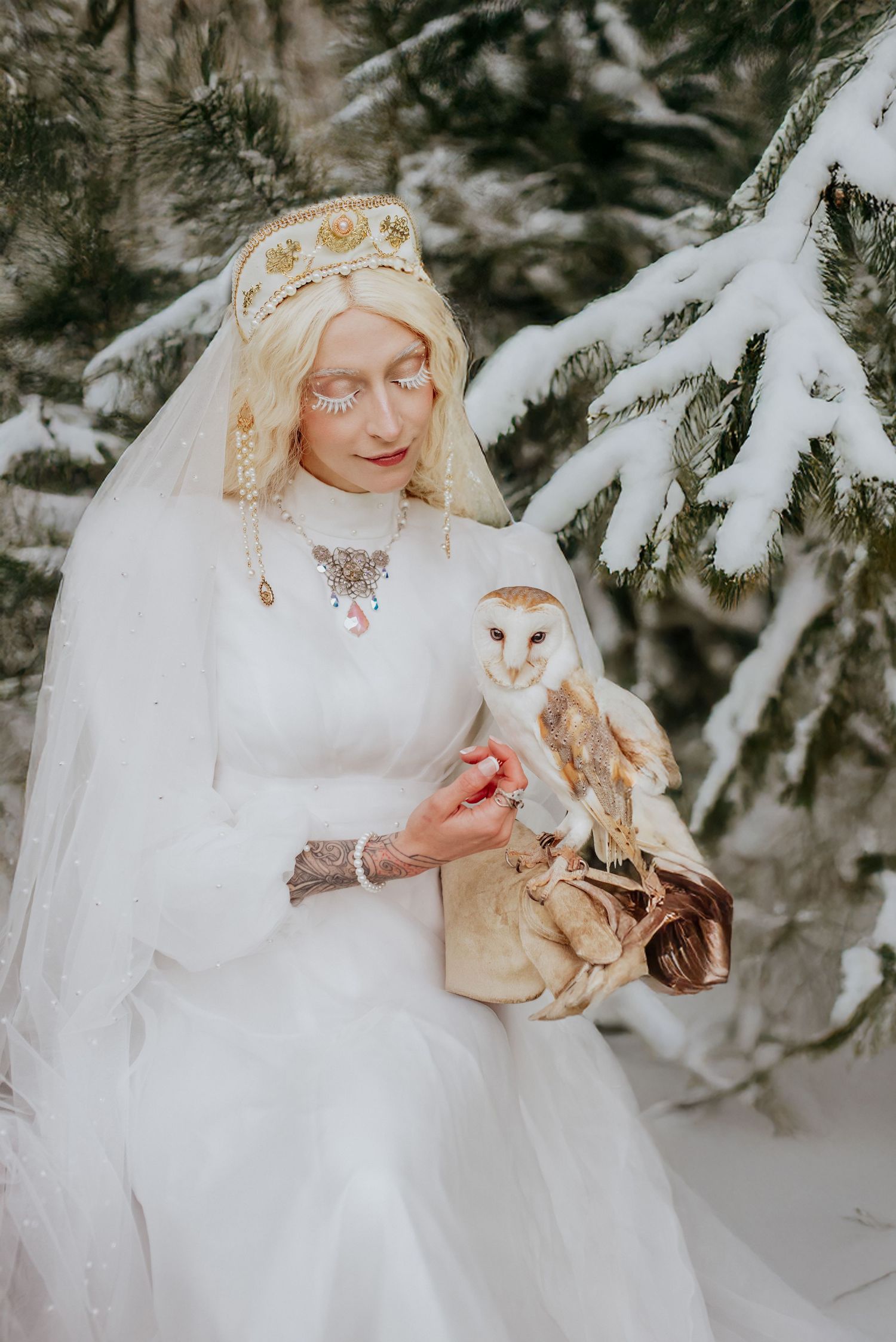 Dreamy winter scene with flowing white dress and snow-covered pine branches in the background.