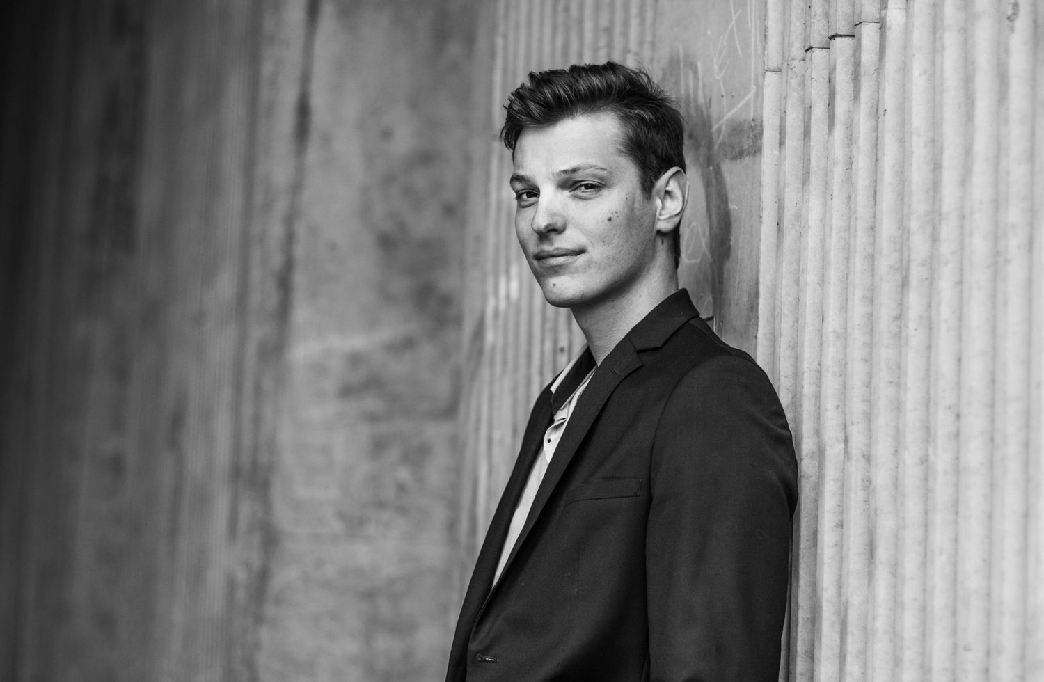 Professional portrait against concrete pillars in black suit.