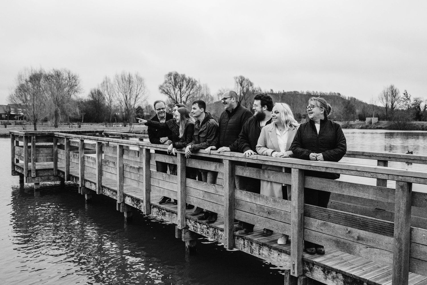 A black and white photo of people standing together on a wooden dock over water.