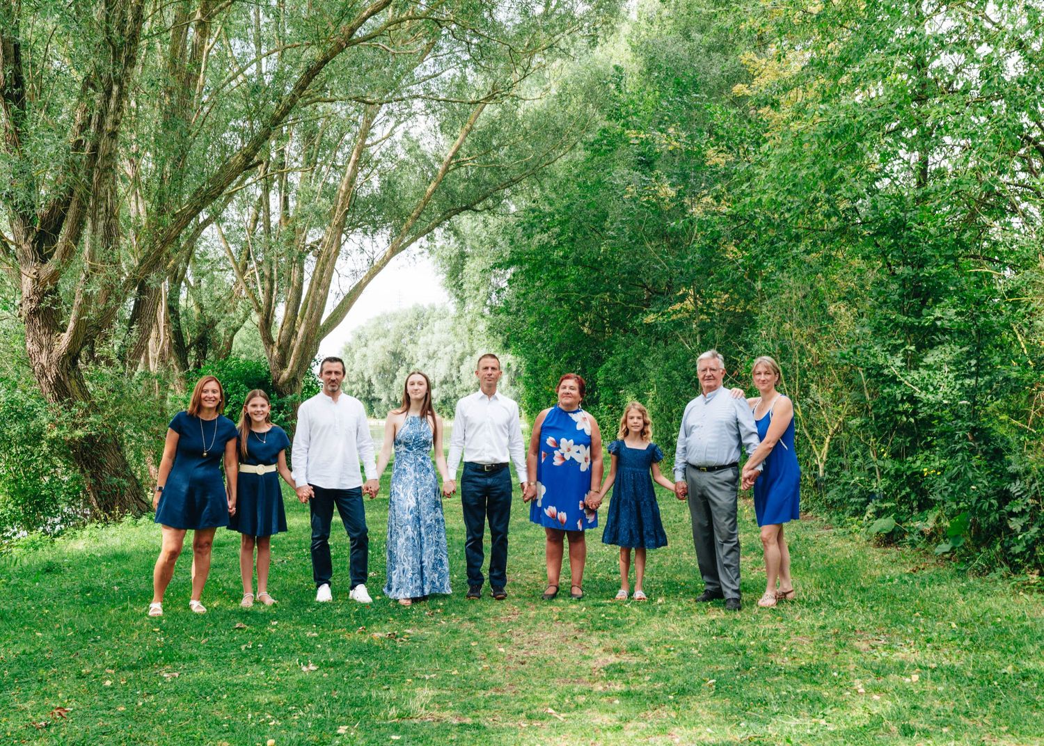 Wide landscape shot of family group standing together in wooded outdoor setting.
