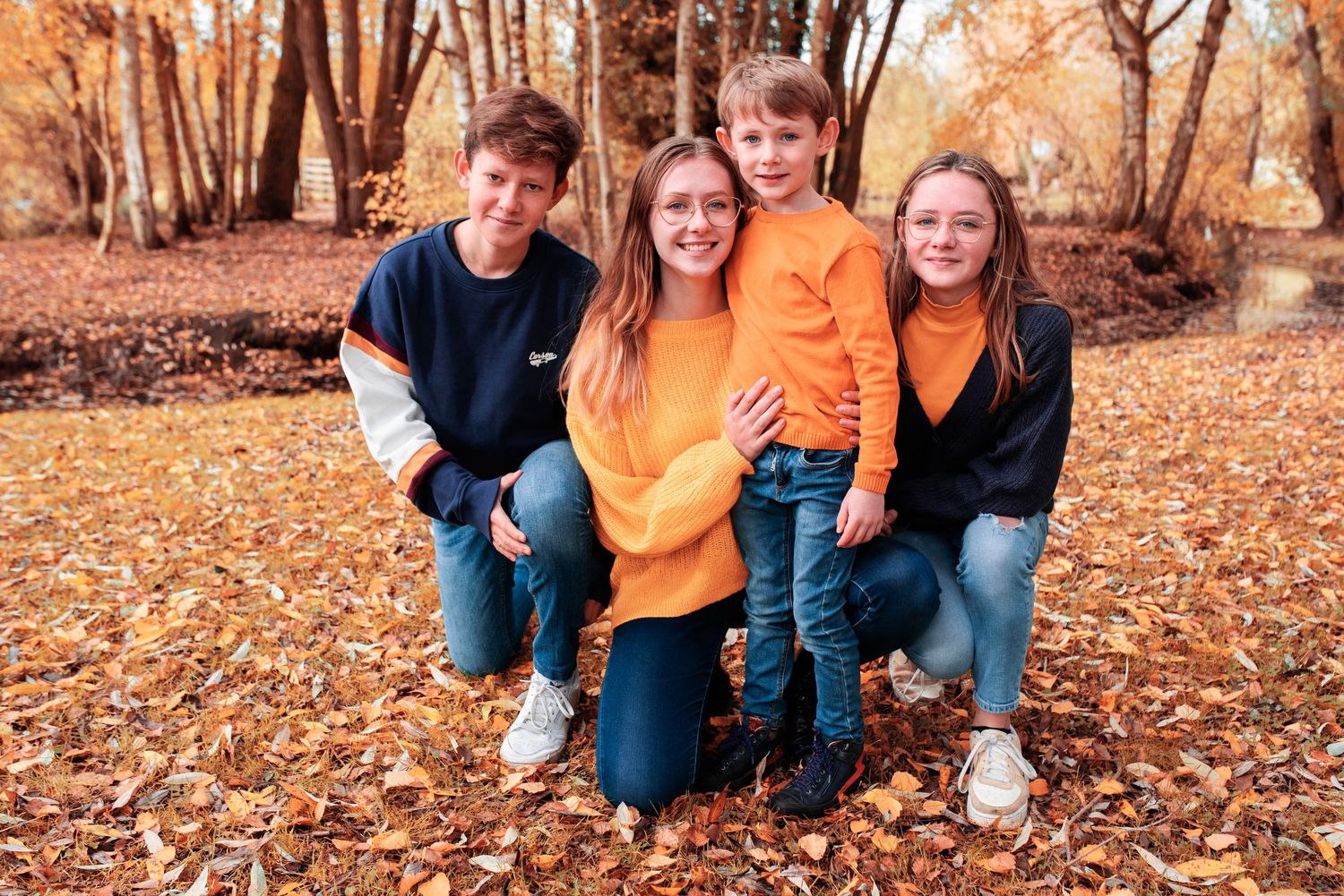Family group portrait in matching orange and navy outfits among autumn foliage.