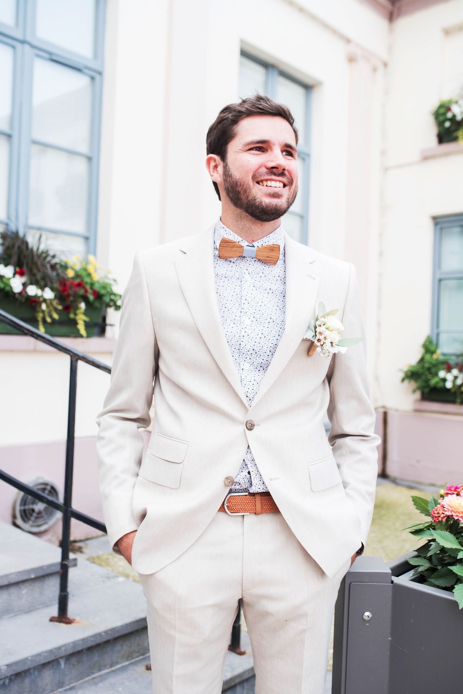 Groom in light colored suit poses confidently on steps outside wedding venue.