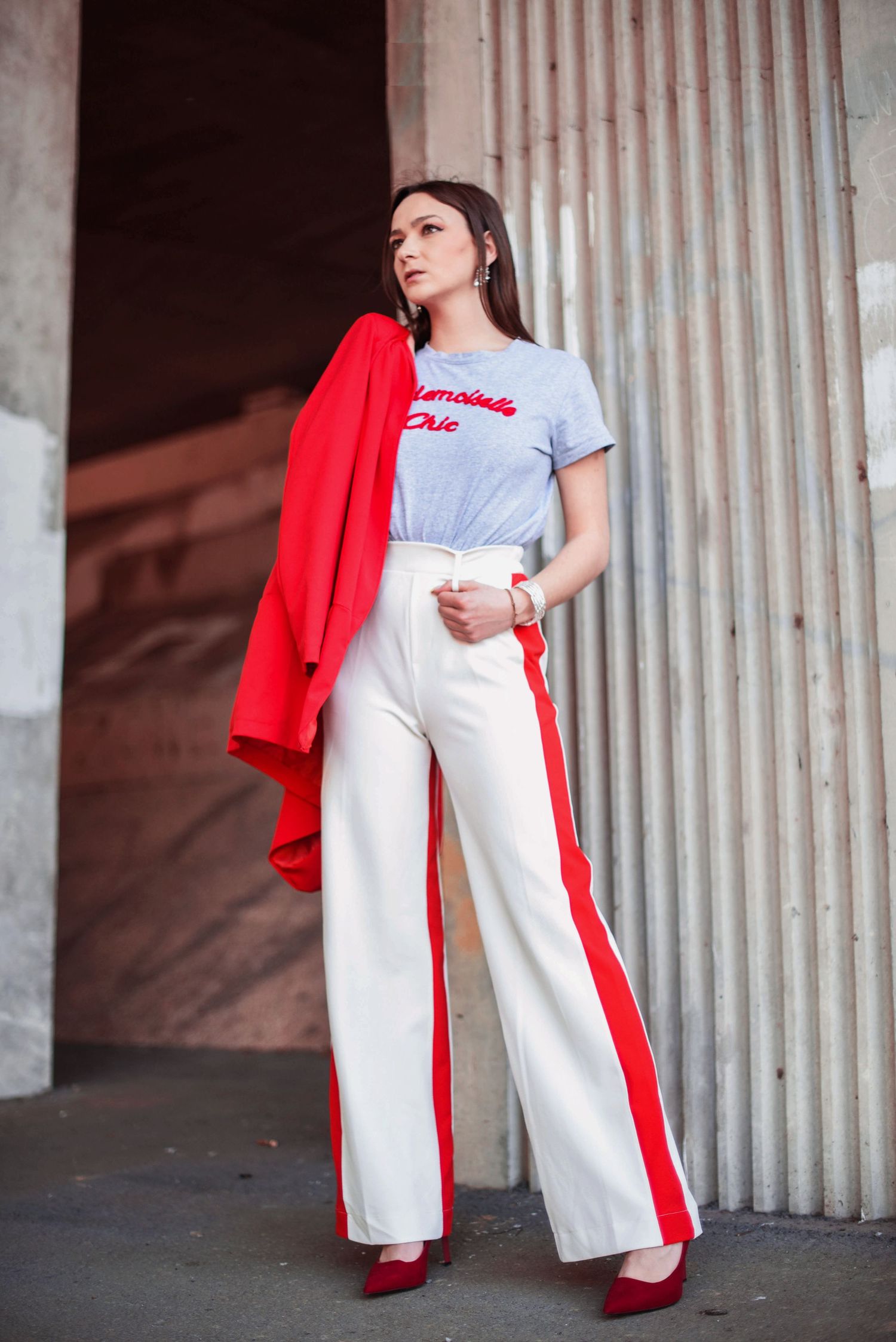 Athletic inspired outfit with red jacket and white pants in industrial setting.