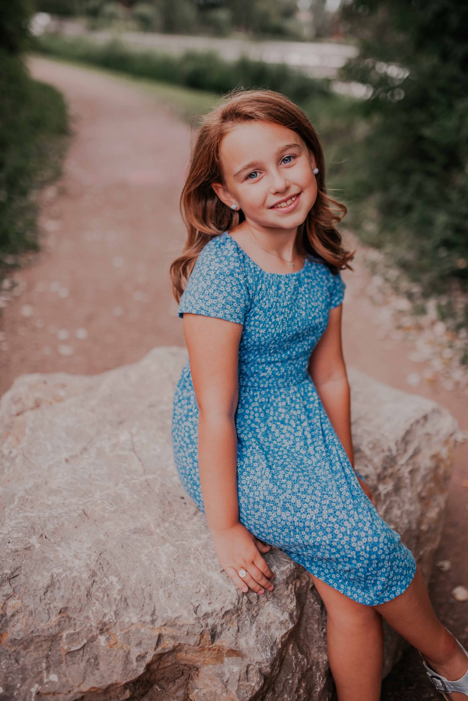 Young person in blue patterned dress poses on rocky surface outdoors.