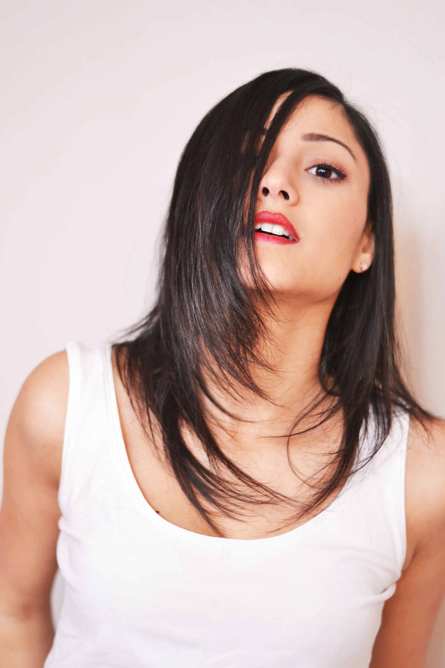Beauty portrait with red lipstick and layered dark hair against white background.