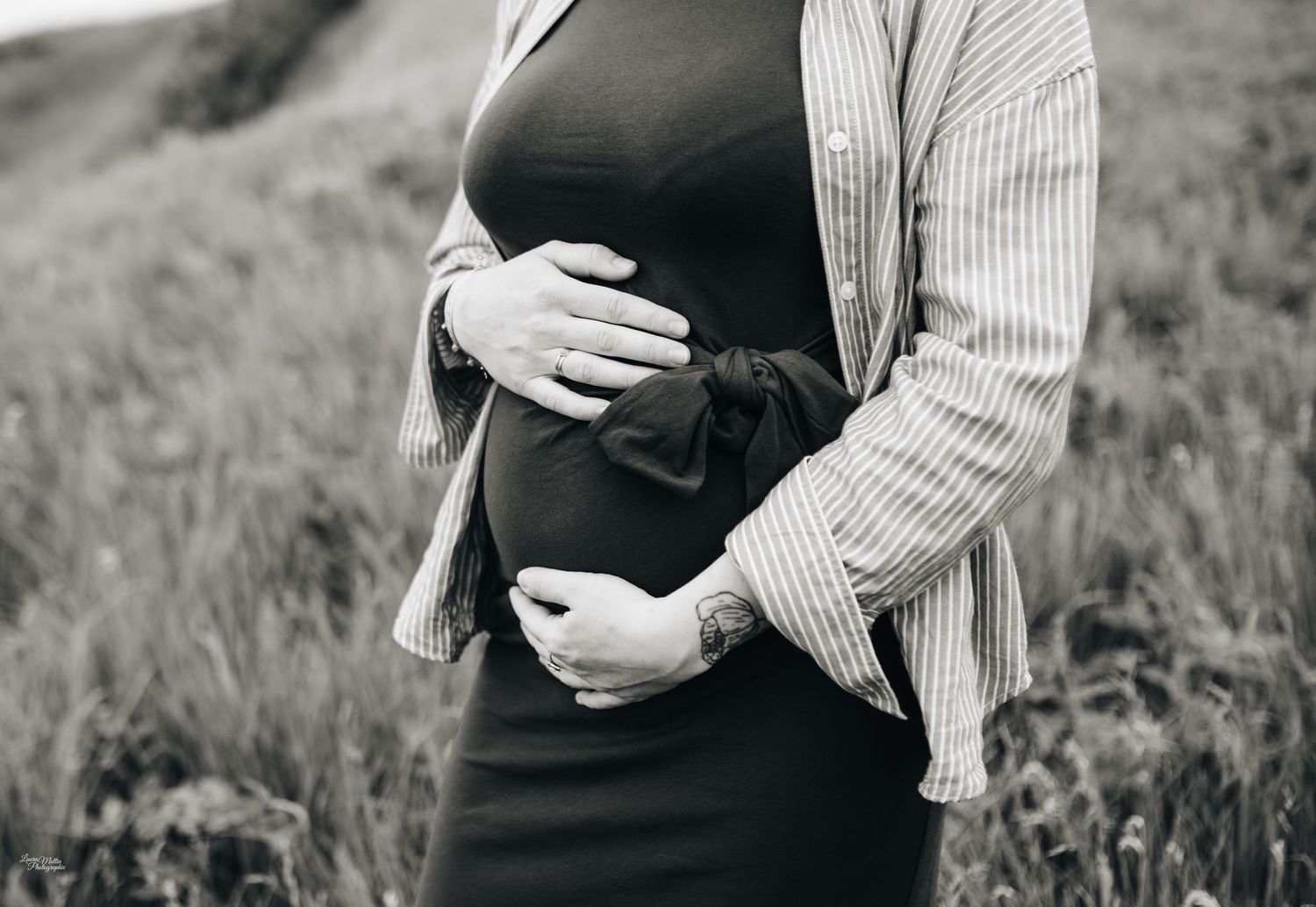 Black and white maternity photo showing gentle embrace against natural backdrop.