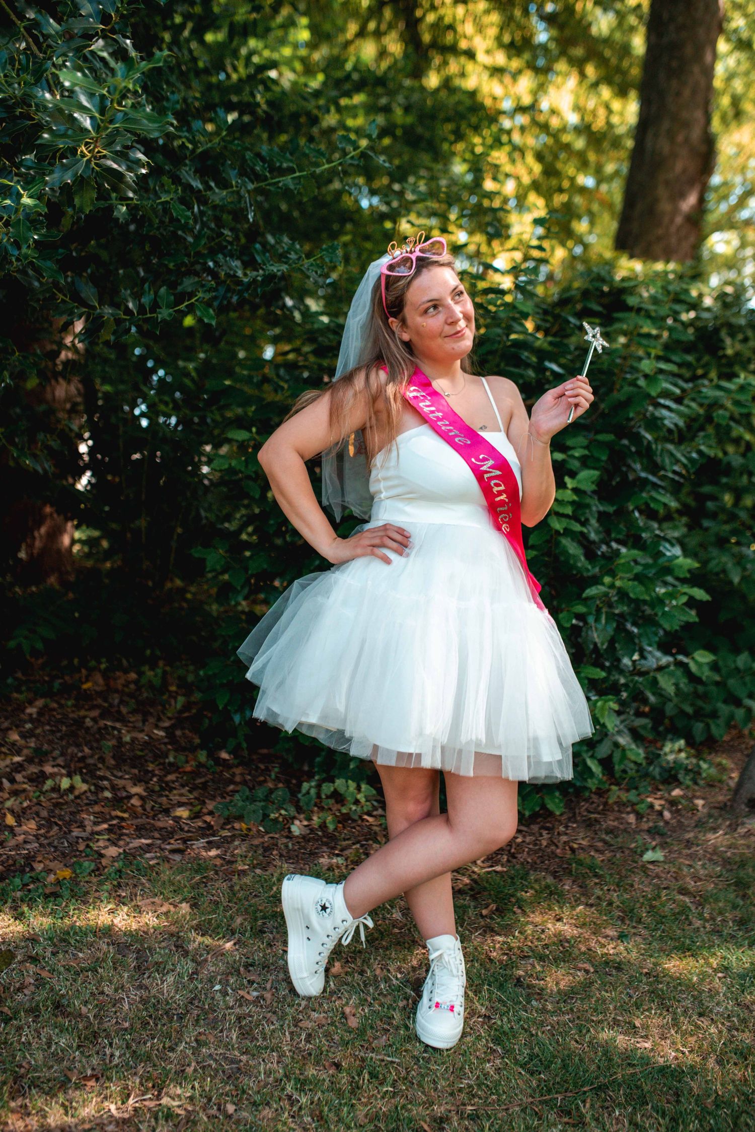A celebratory scene in a garden featuring a white tulle dress, pink sash, and flower crown.