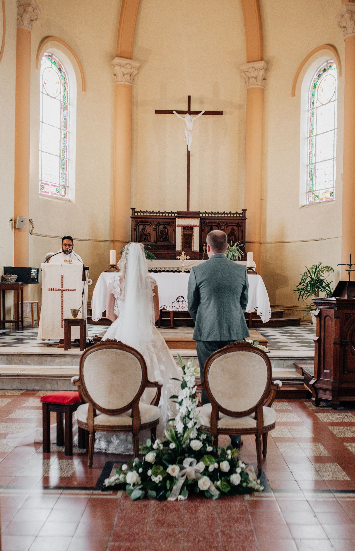 Church interior with altar, cross, and floral arrangements during wedding ceremony.