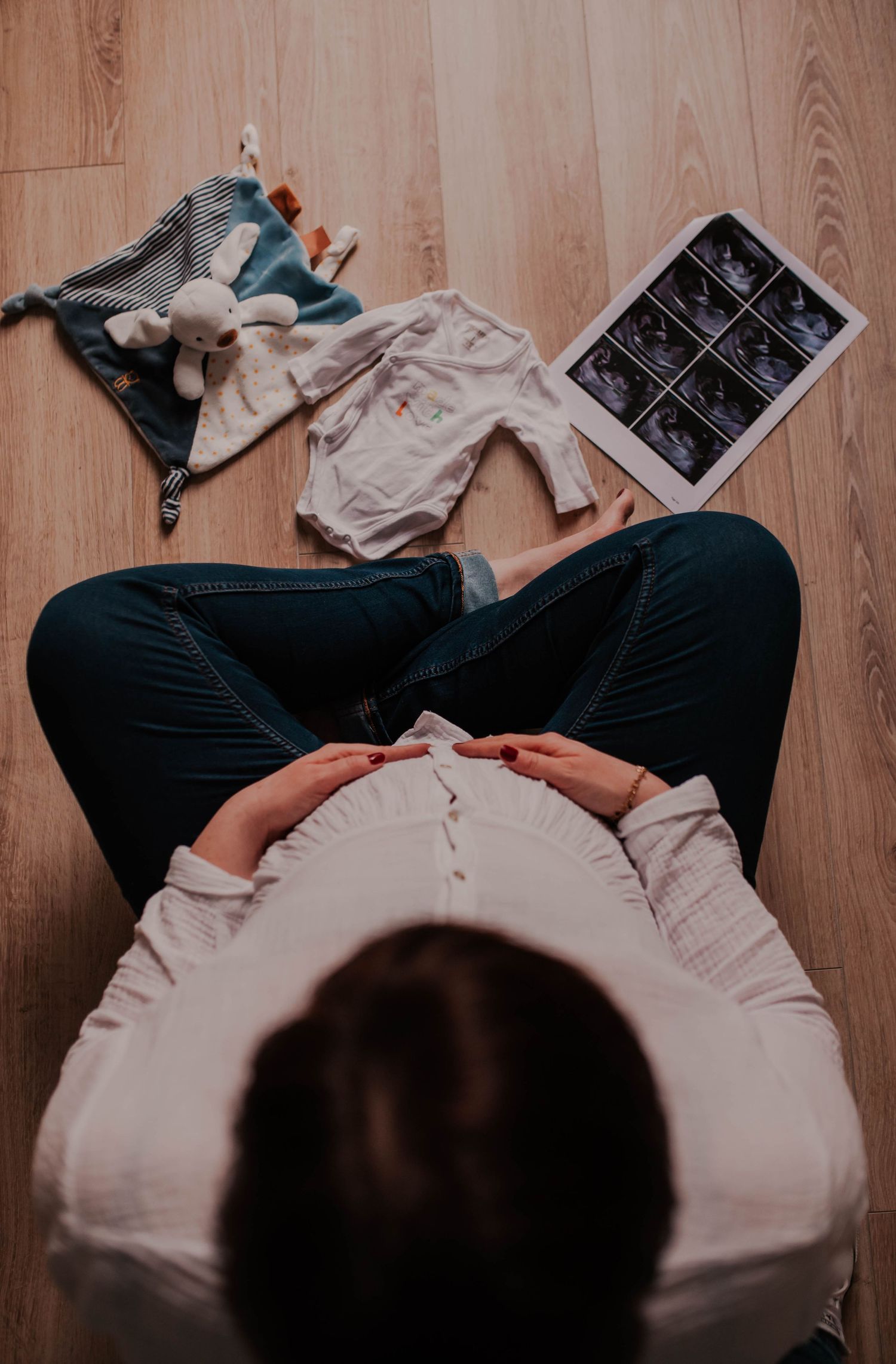 An overhead view of baby items and ultrasound photos arranged on wooden floor.
