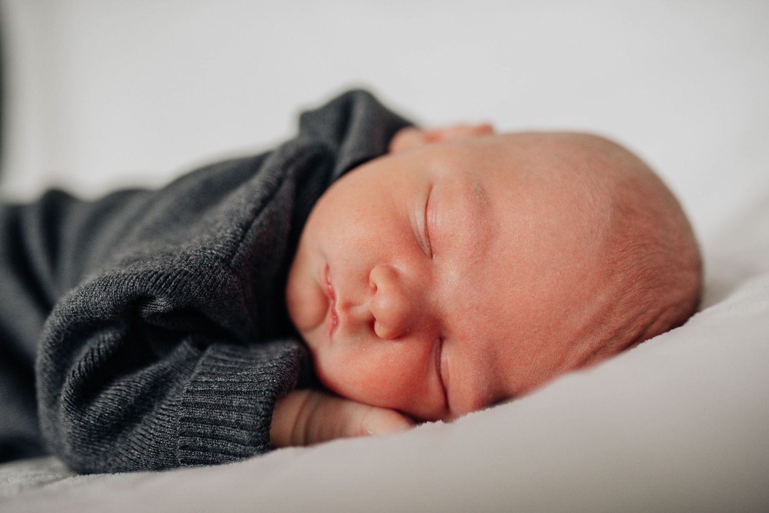 Close-up portraits of sleeping newborn baby in dark sweater on white background.