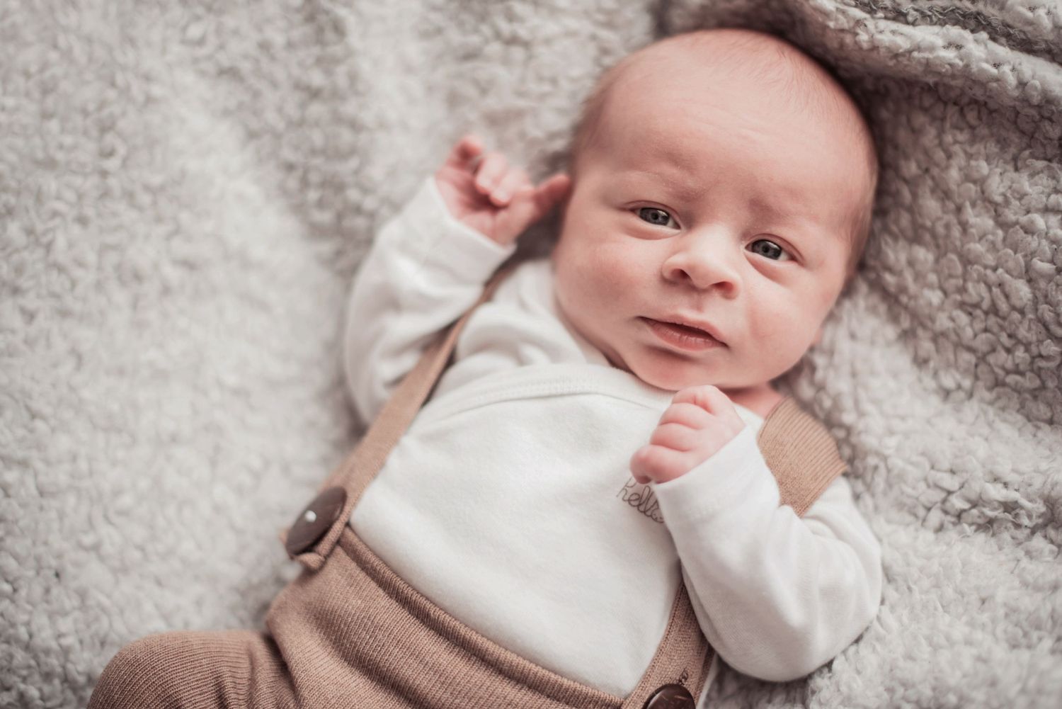 Sweet portrait series of baby in white clothing resting on textured gray blanket.