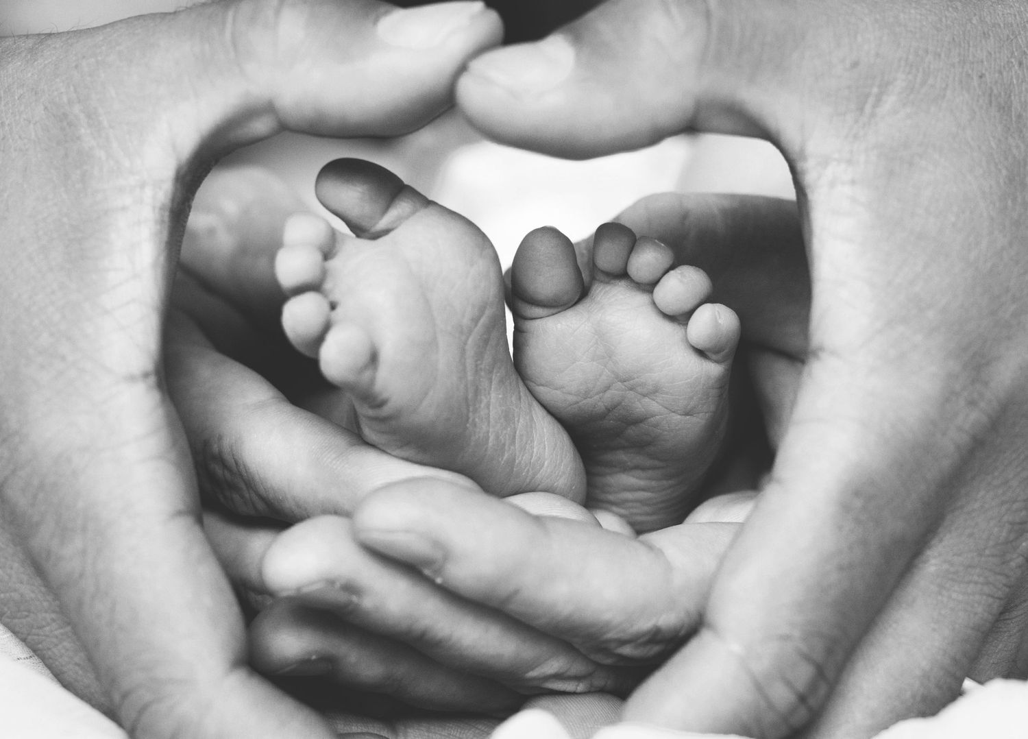 Close-up black and white photos of small baby feet being held in caring hands.