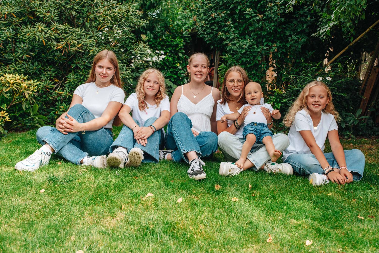 A group sits together on green grass wearing coordinated white tops and blue jeans.