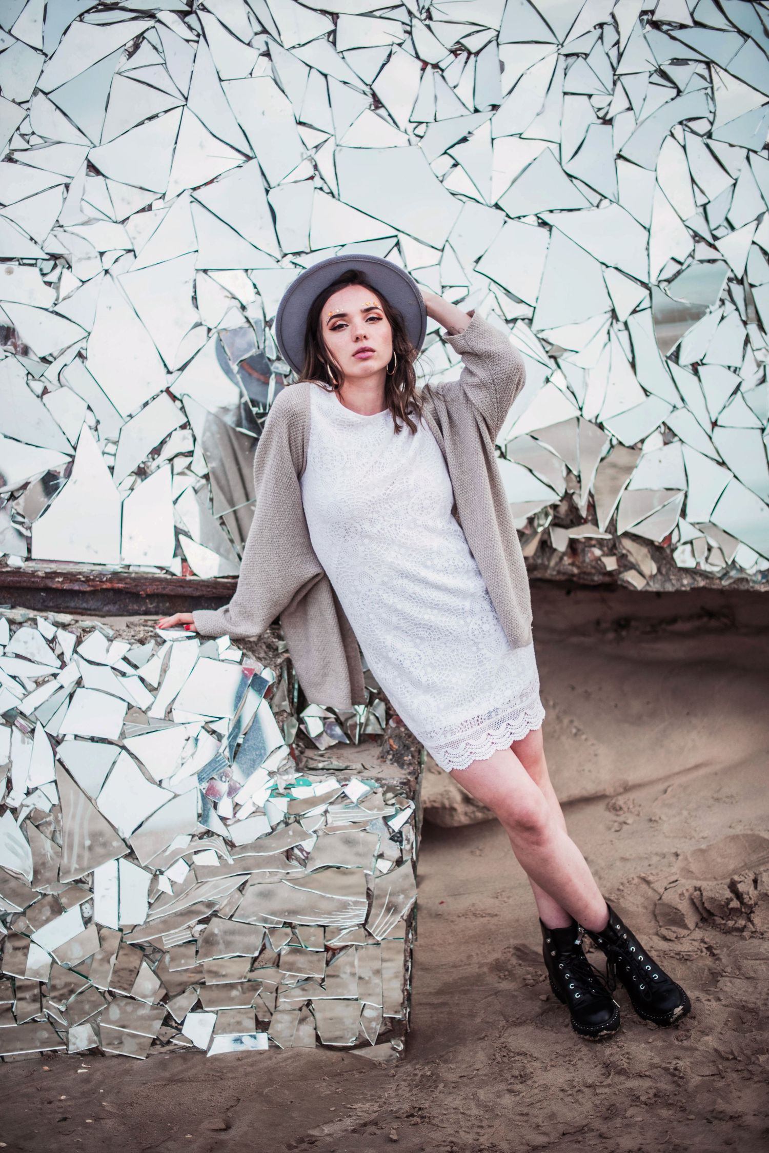 Fashion portrait against a mirrored wall backdrop wearing a white dress and gray coat.