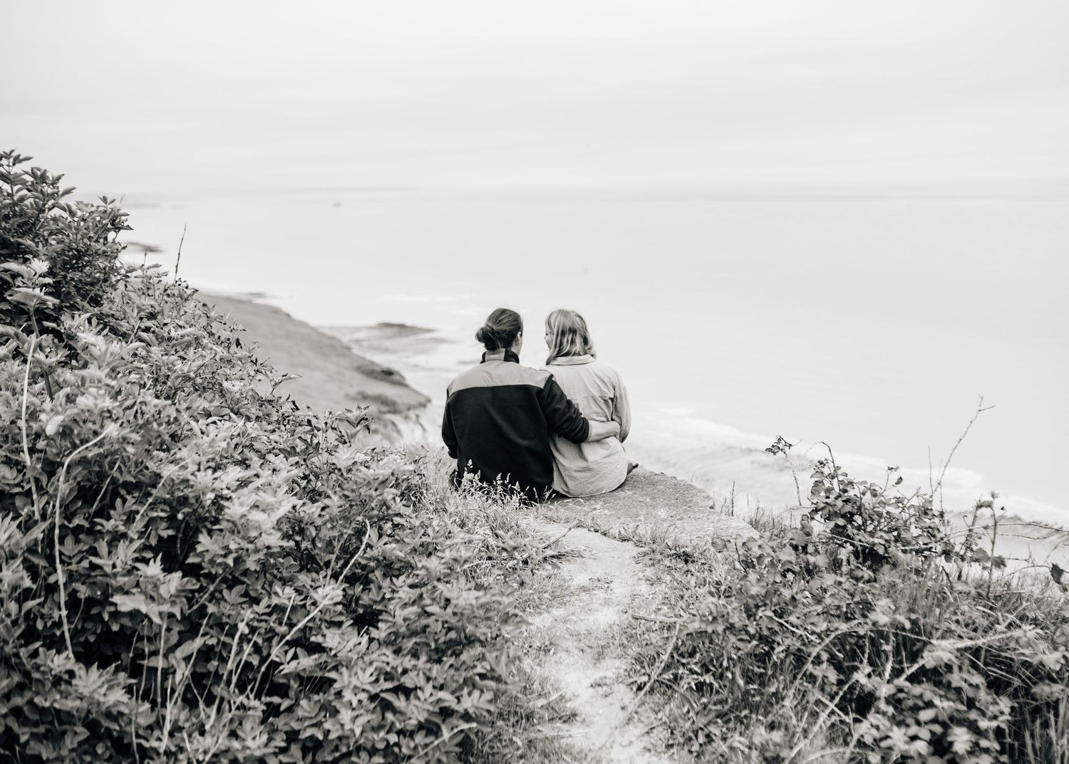 A series of silhouettes against a bright sky showing a couple walking along a scenic coastal path.
