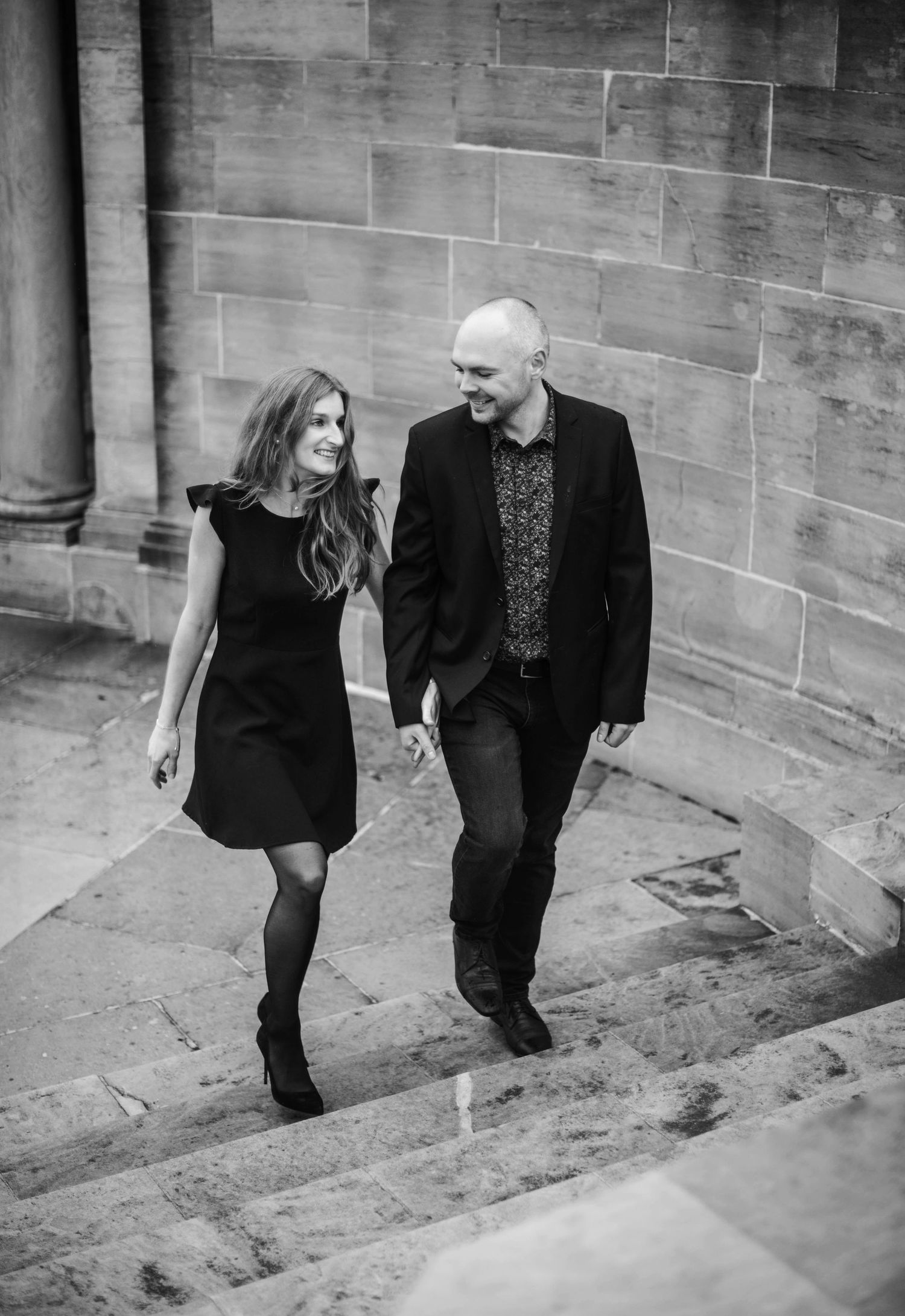 Couple walking together along stone wall in artistic black and white sequence.