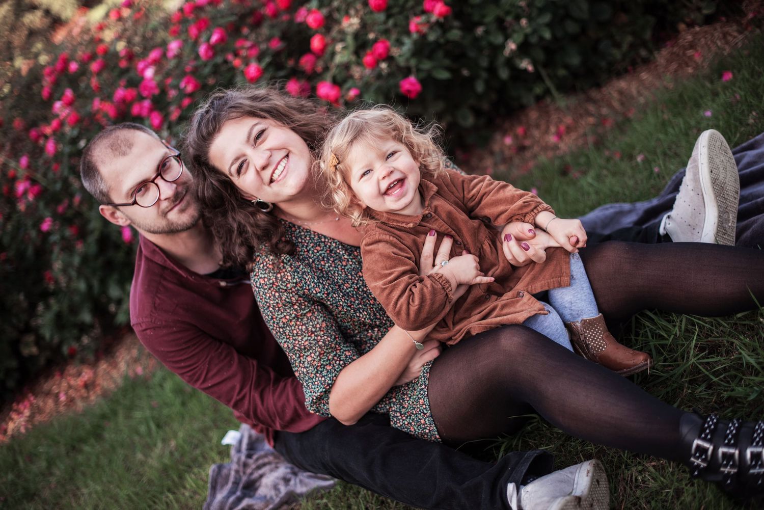 Family members laughing together on grass with pink flowers in background.