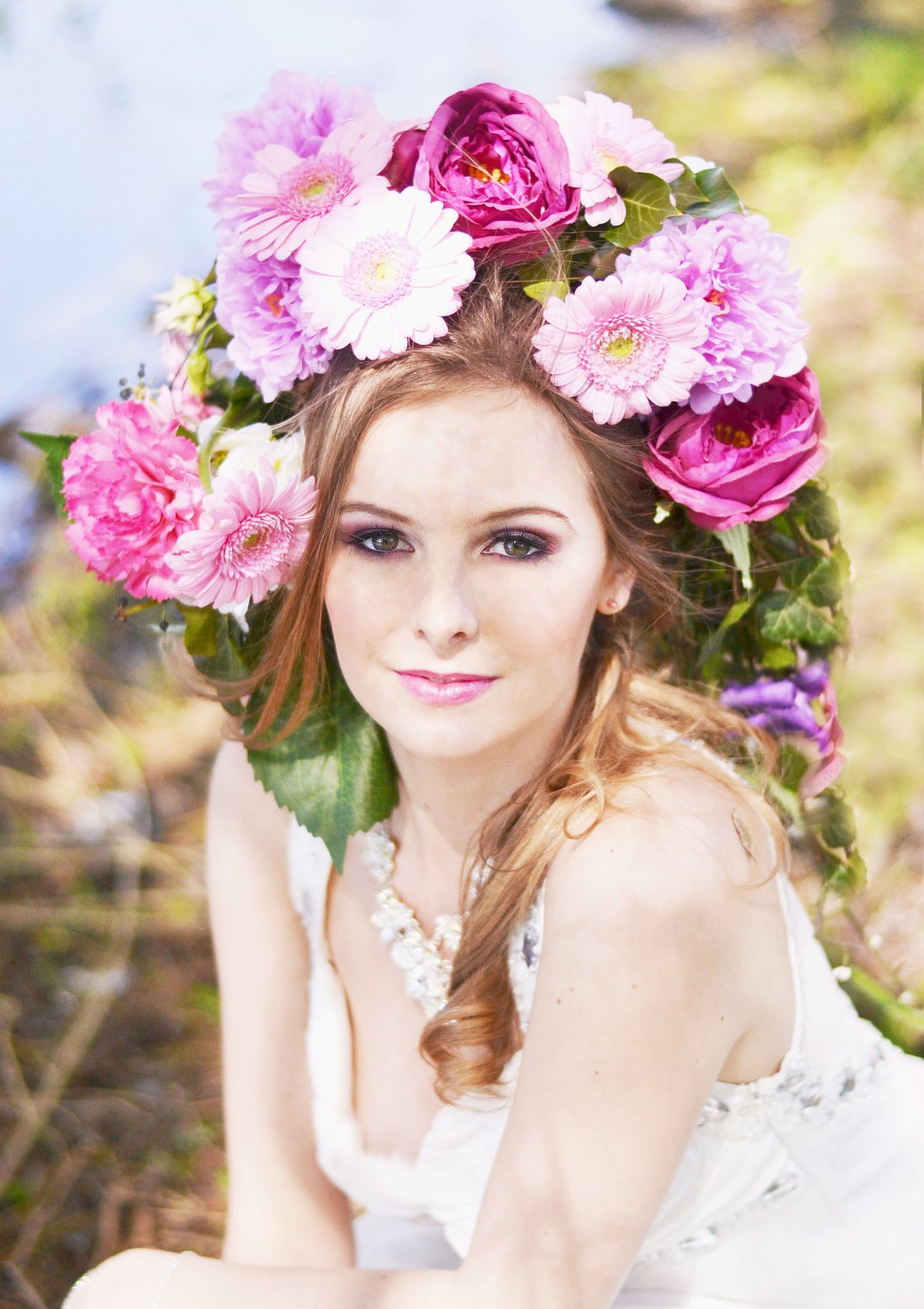 Romantic portrait with pink floral crown and white lace dress in soft lighting.