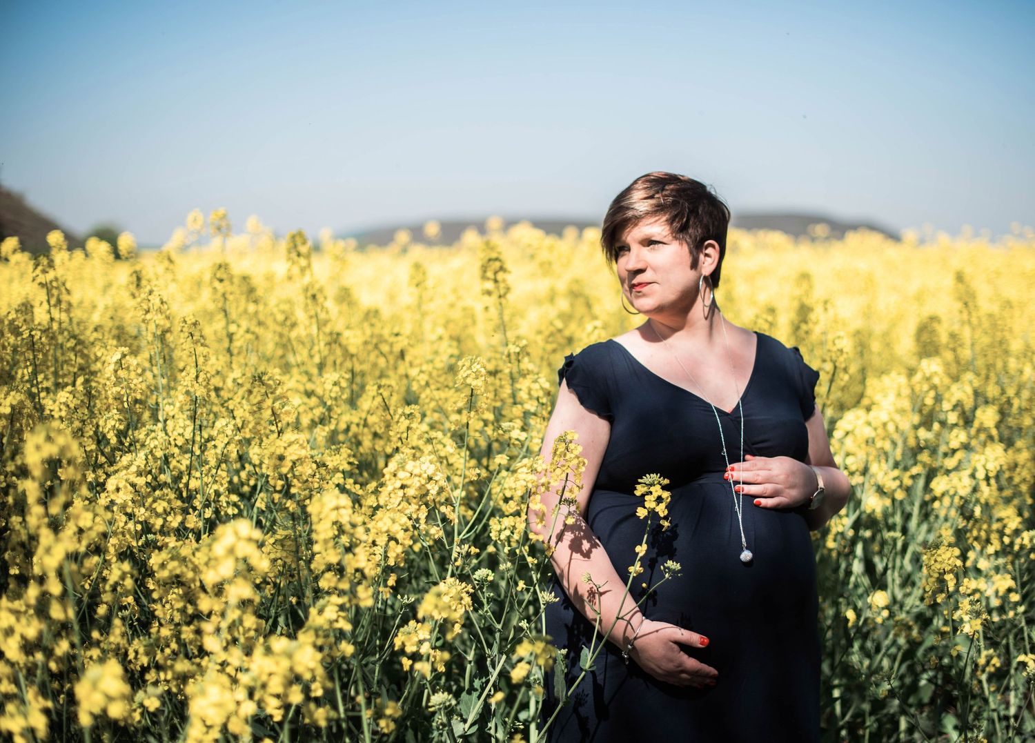 Maternity photo in a vibrant yellow canola field on a sunny day.