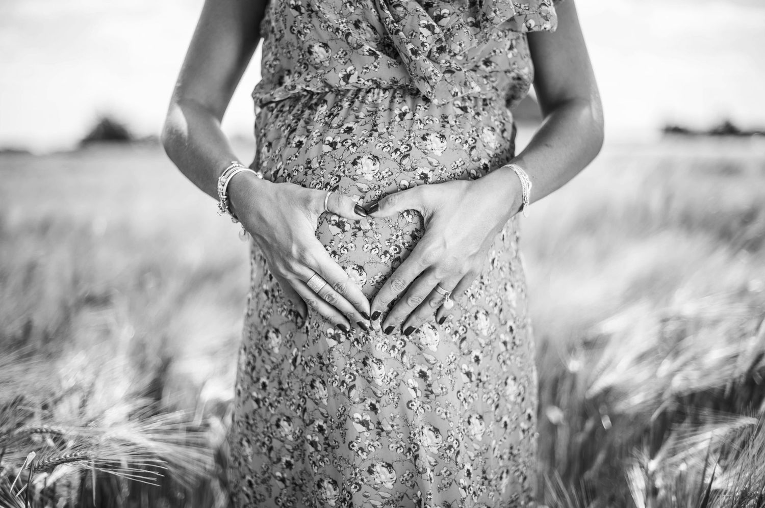 Black and white maternity portrait in floral dress against natural backdrop.