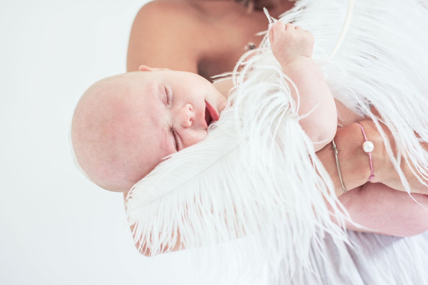 Artistic white high-key portraits of a sleeping newborn wrapped in soft fabric.