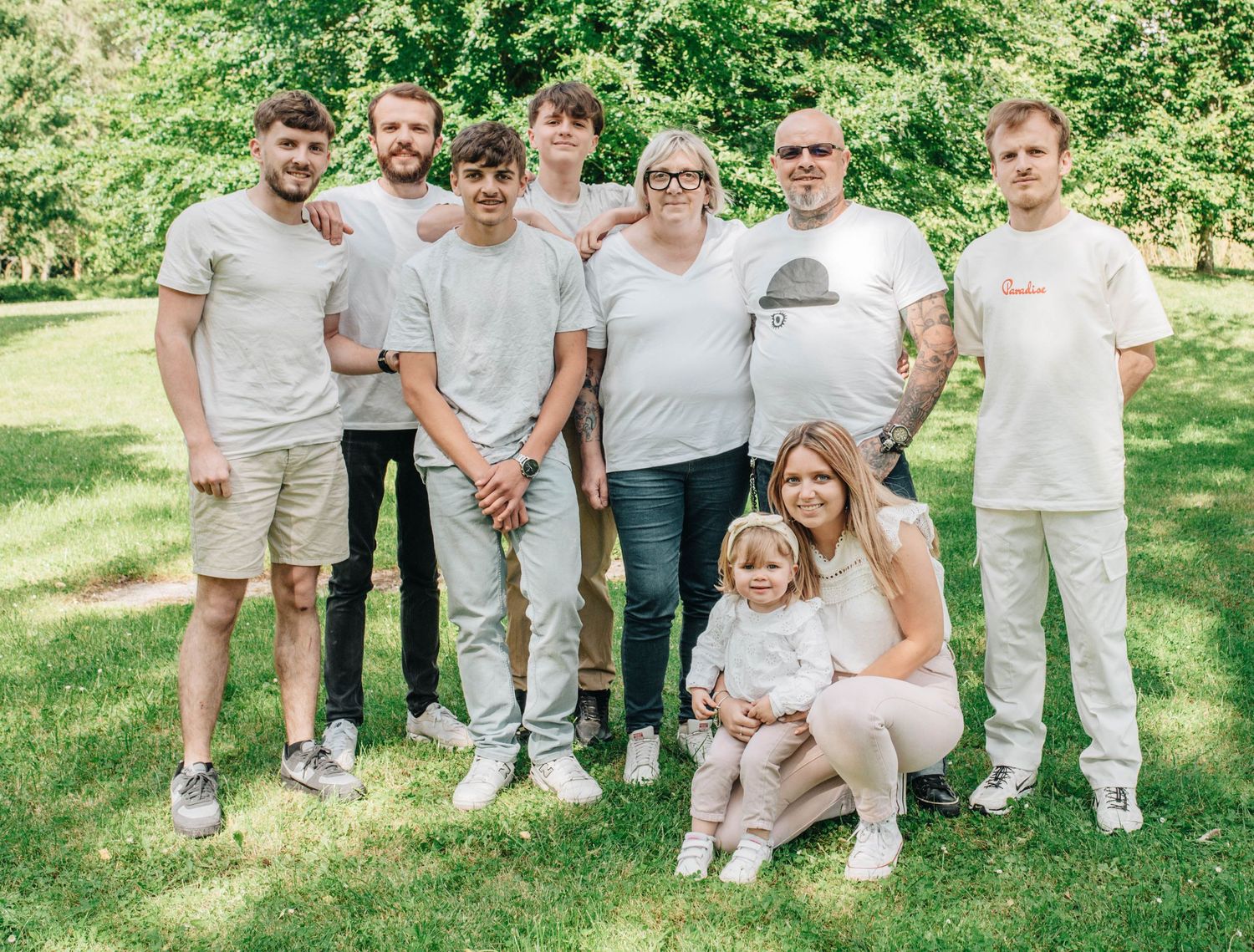 Extended family group portrait in coordinating white and grey outfits on sunny lawn.