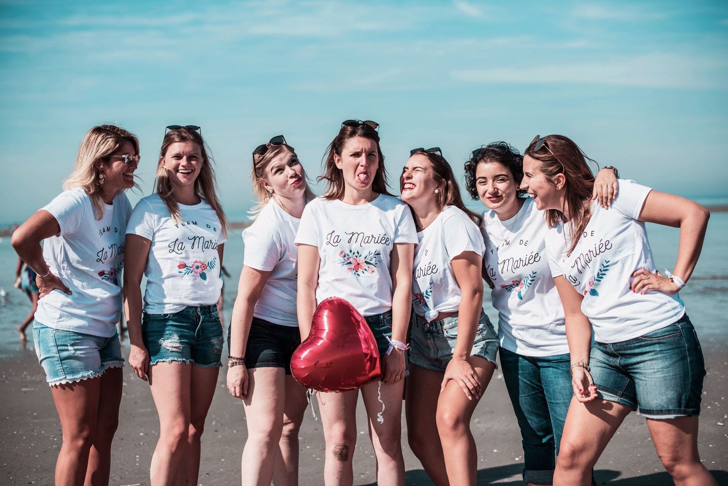 Friends in coordinated outfits pose for fun beach photo series.