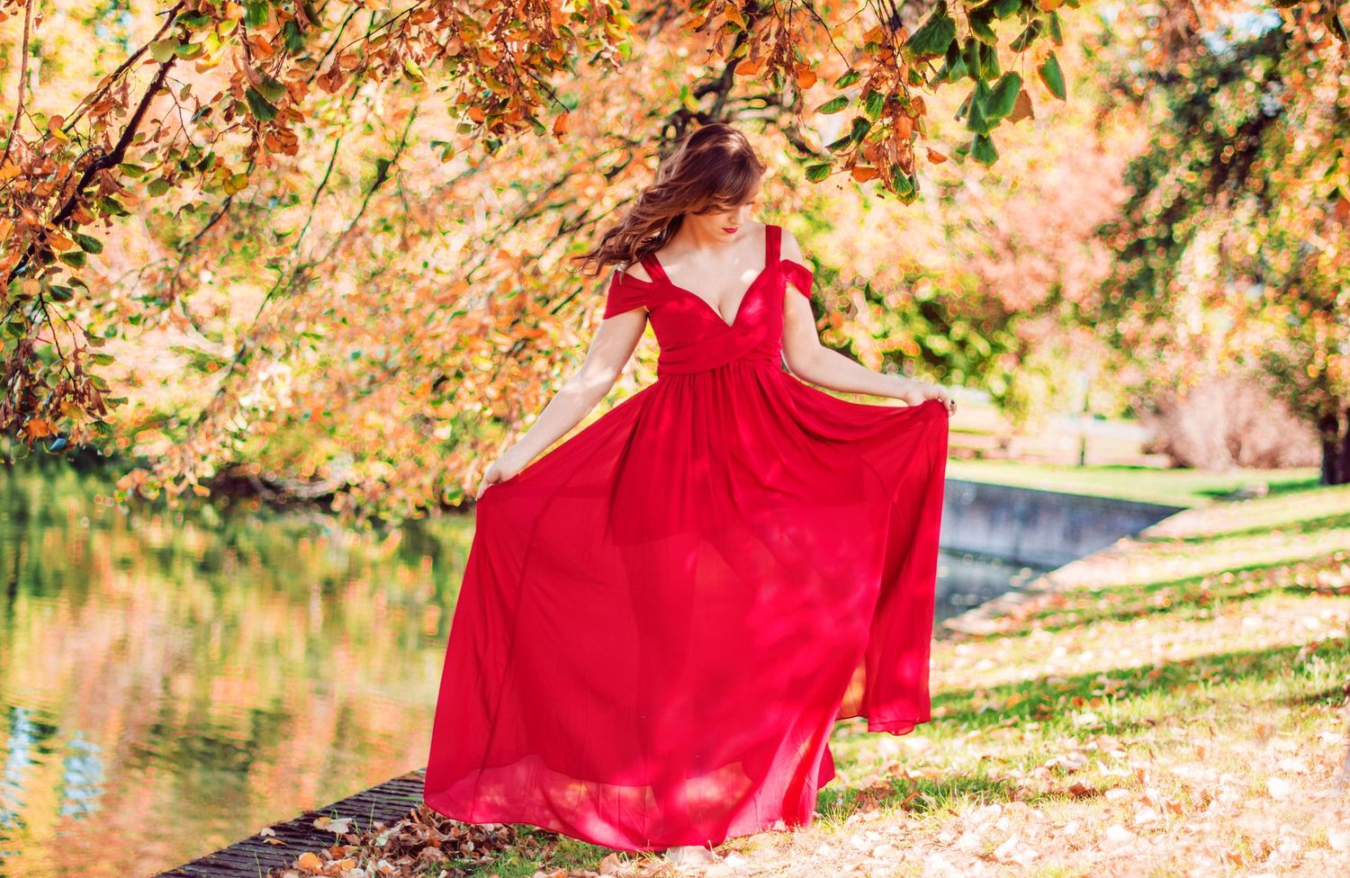 Red dress contrasts beautifully with autumn foliage by lake.