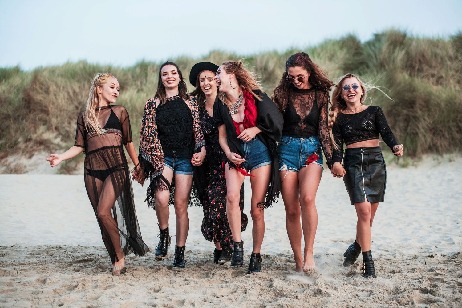 Group walking together on a sandy beach at sunset showing just their legs and feet.
