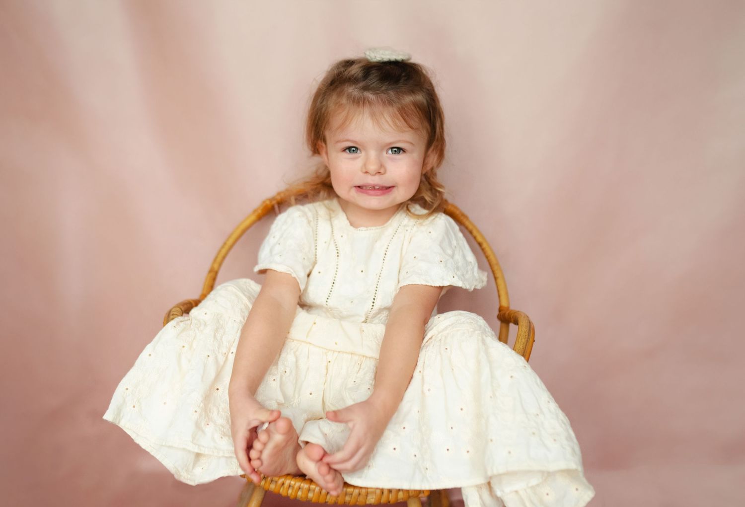 Multiple portrait shots of a young child in a white dress against a soft pink studio backdrop.