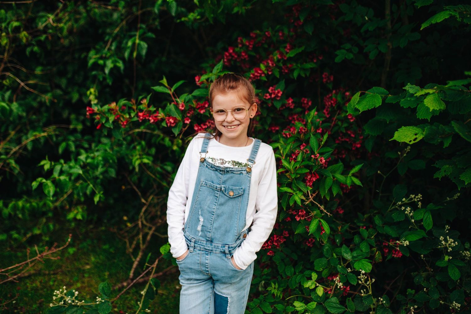 Outdoor portrait series featuring someone in overalls against flowering bushes and greenery.
